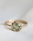 Gold ring with a green gemstone on a white fabric background