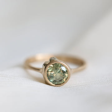 Gold ring with a green gemstone on a white fabric background