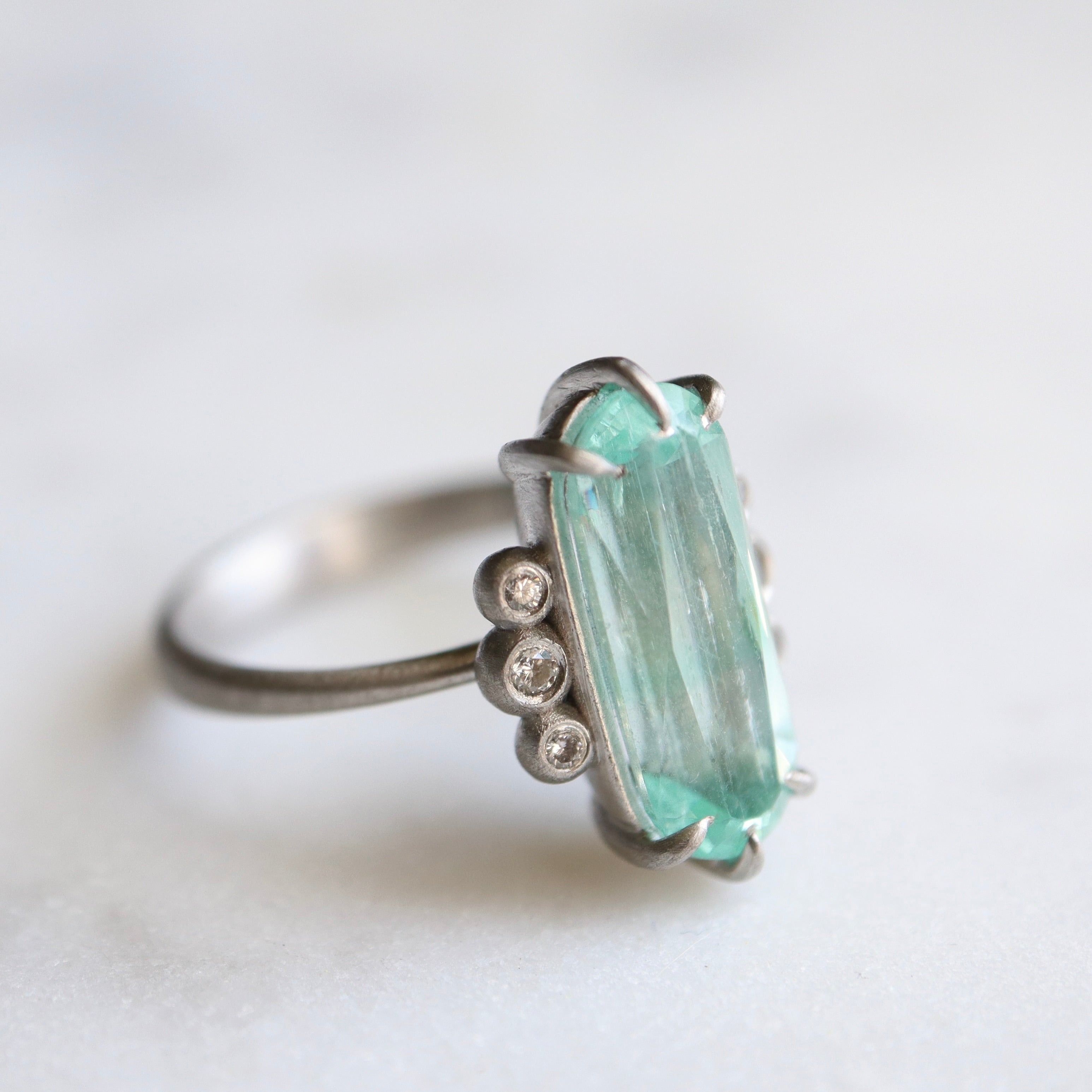 oval emerald center stone with three diamonds on each side. set in platinum. side view.