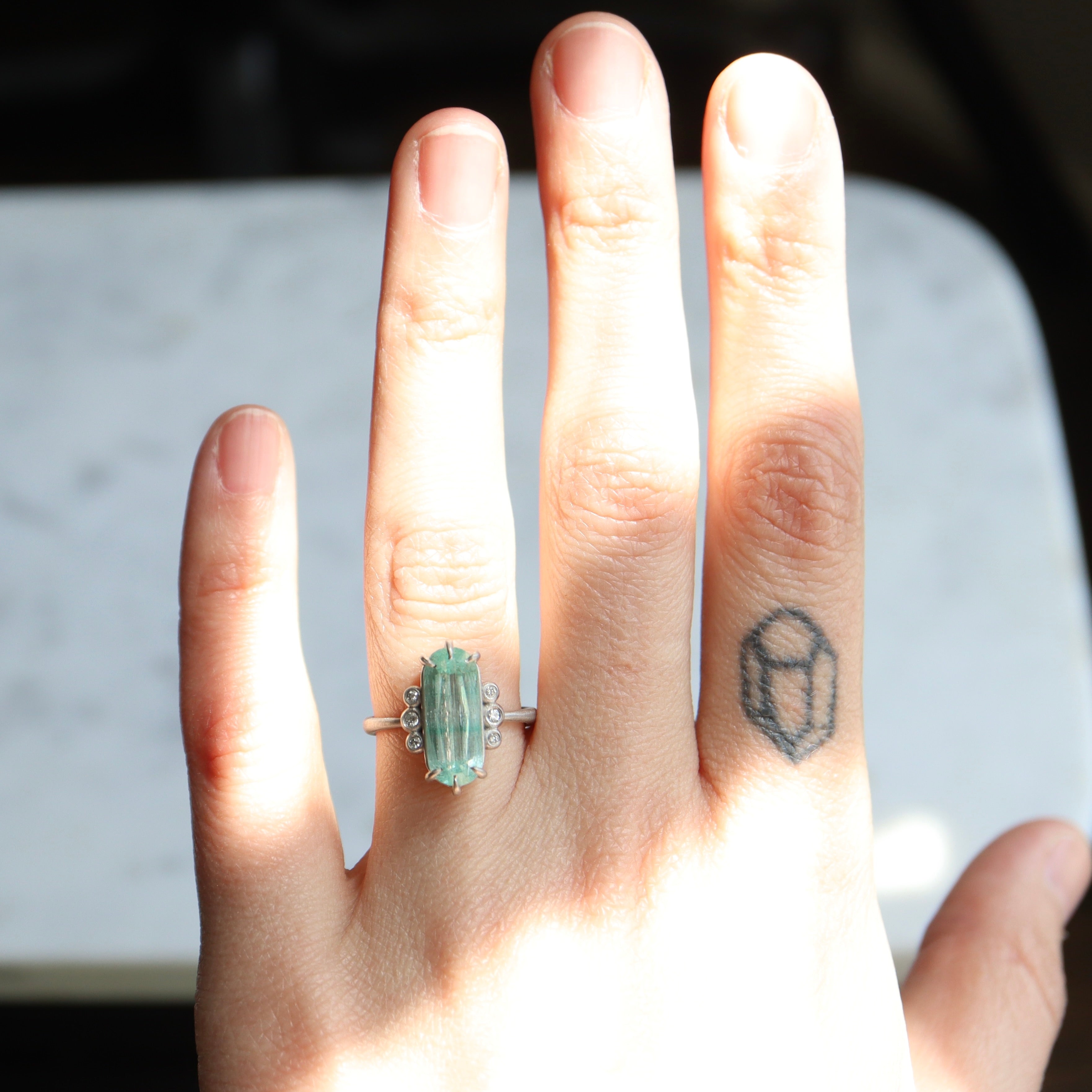 oval emerald center stone with three diamonds on each side. set in platinum. on person