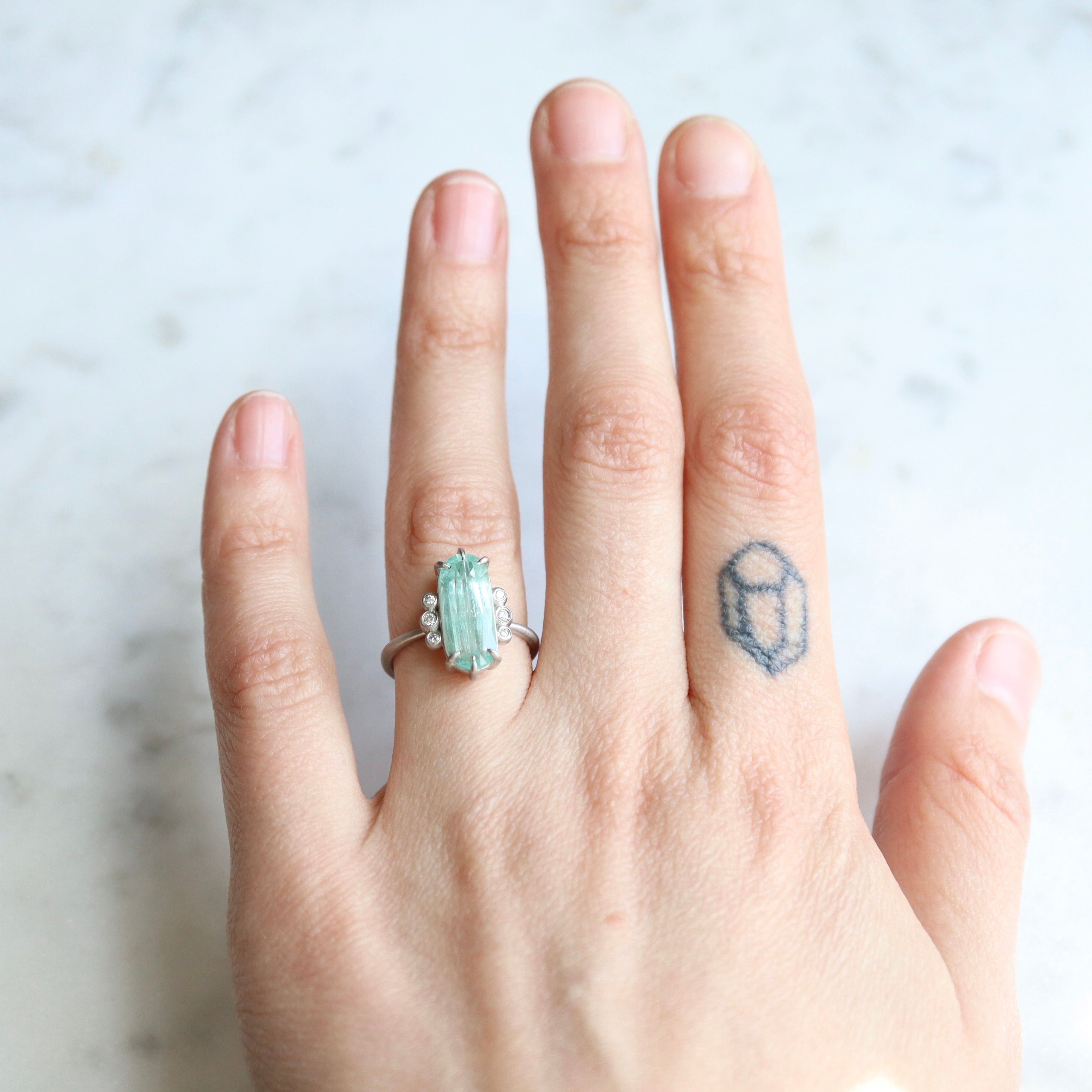 oval emerald center stone with three diamonds on each side. set in platinum. on person.