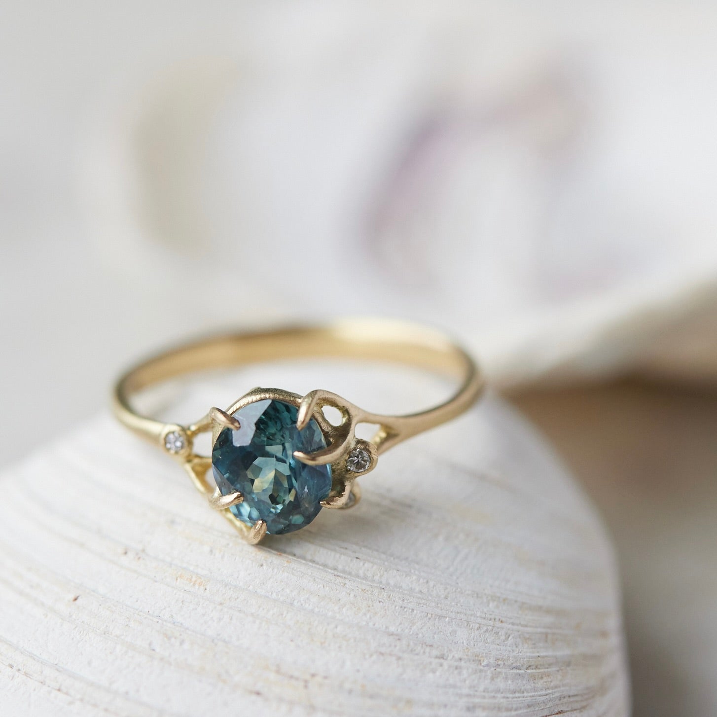 oval teal montana sapphire is set in a gold branch ring with vine-like prongs holding the stone in. Three little diamond berries adorn the branches. Front view.