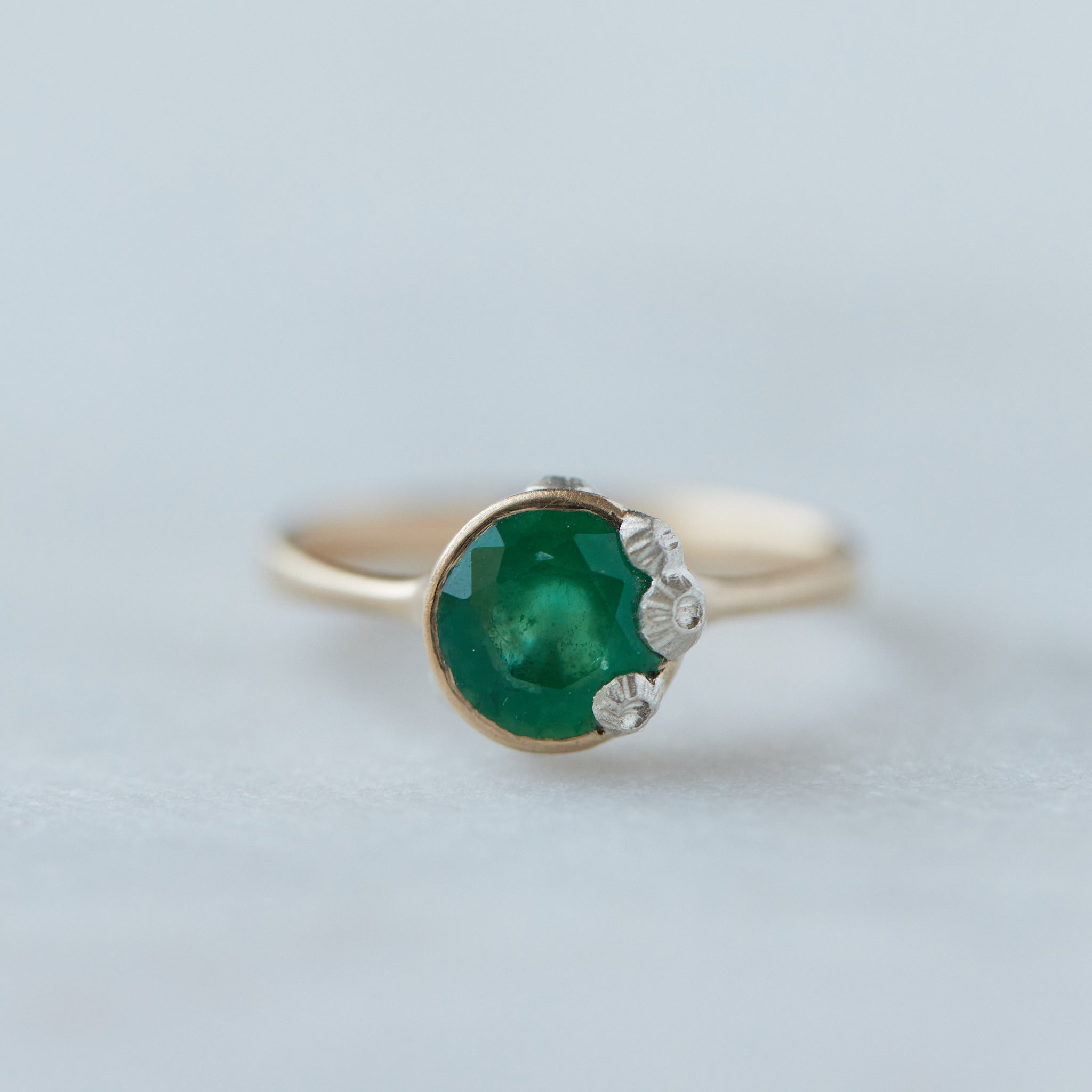 rich green stone set in gold bezel ring with silver barnacles around the rim. Front view.