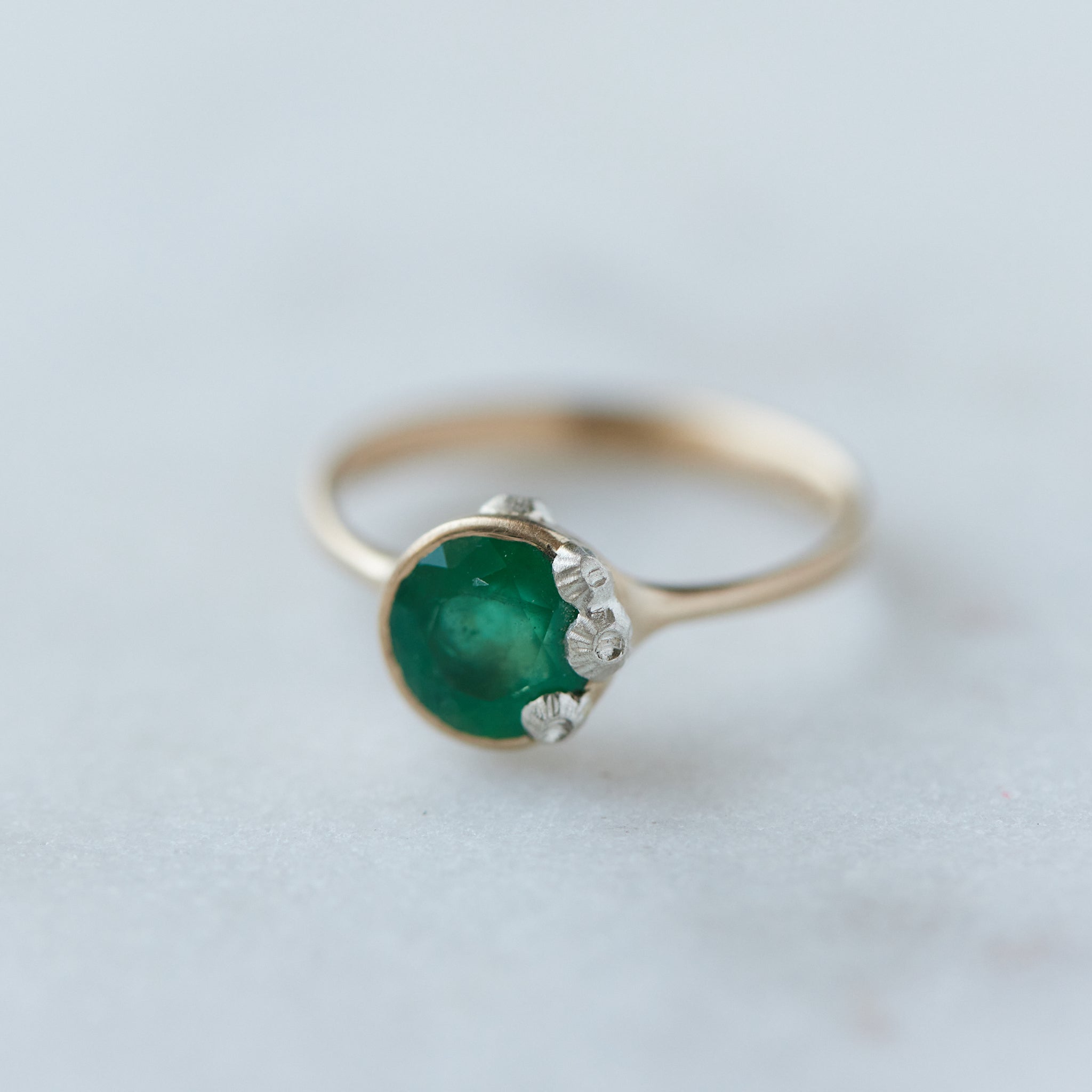 rich green stone set in gold bezel ring with silver barnacles around the rim. 1/4 view.