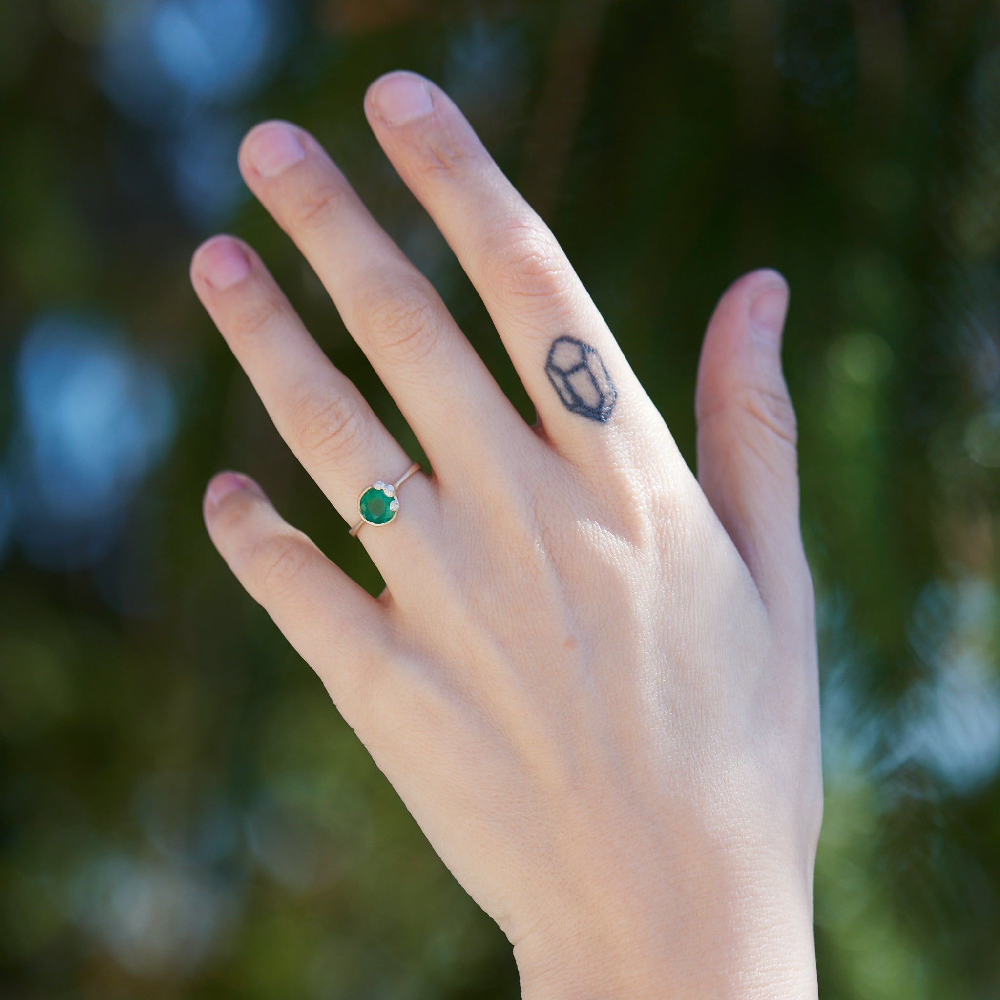 rich green stone set in gold bezel ring with silver barnacles around the rim. Photographed on hand.