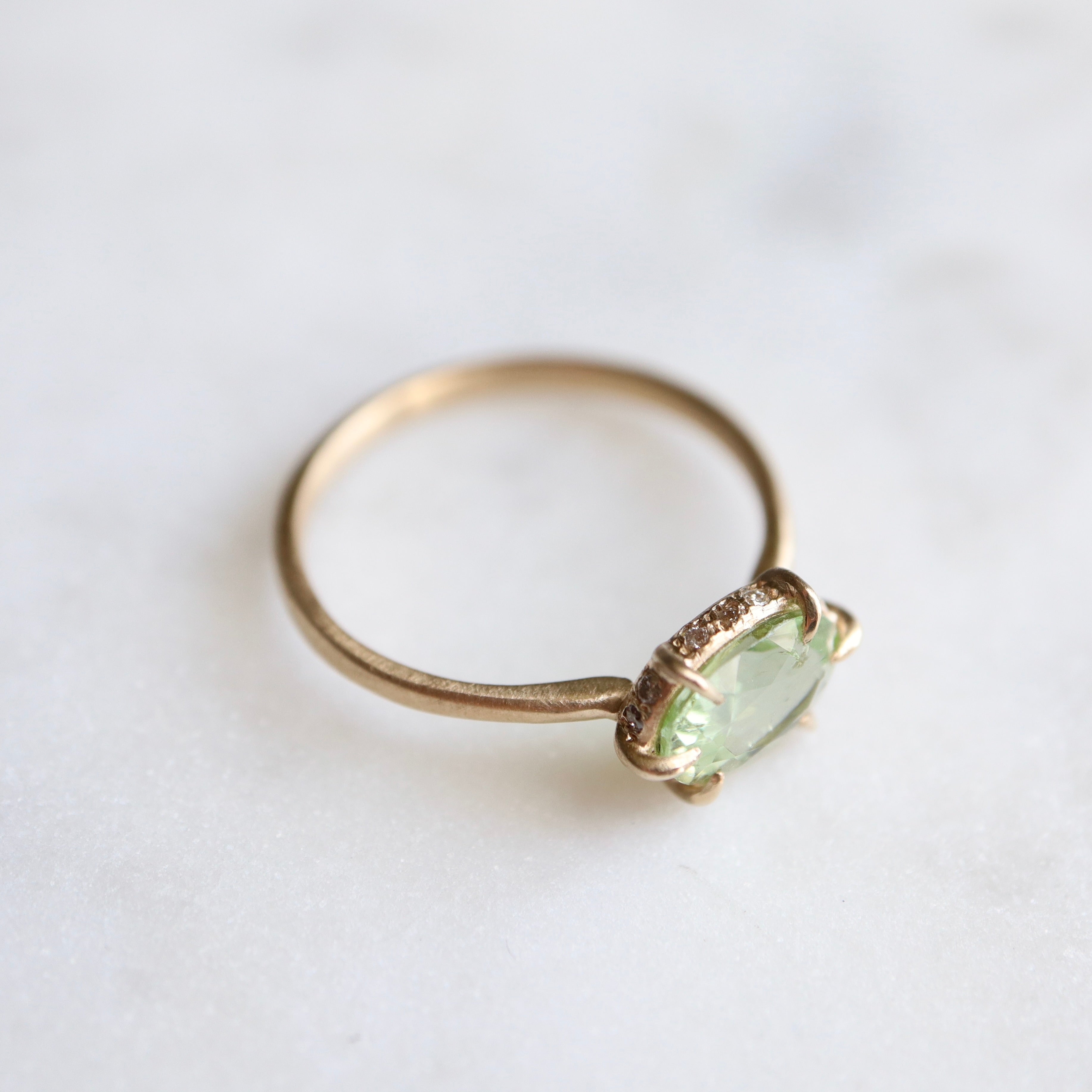 green oval tourmaline ring with gold prongs with diamonds set on side of the setting. side view.