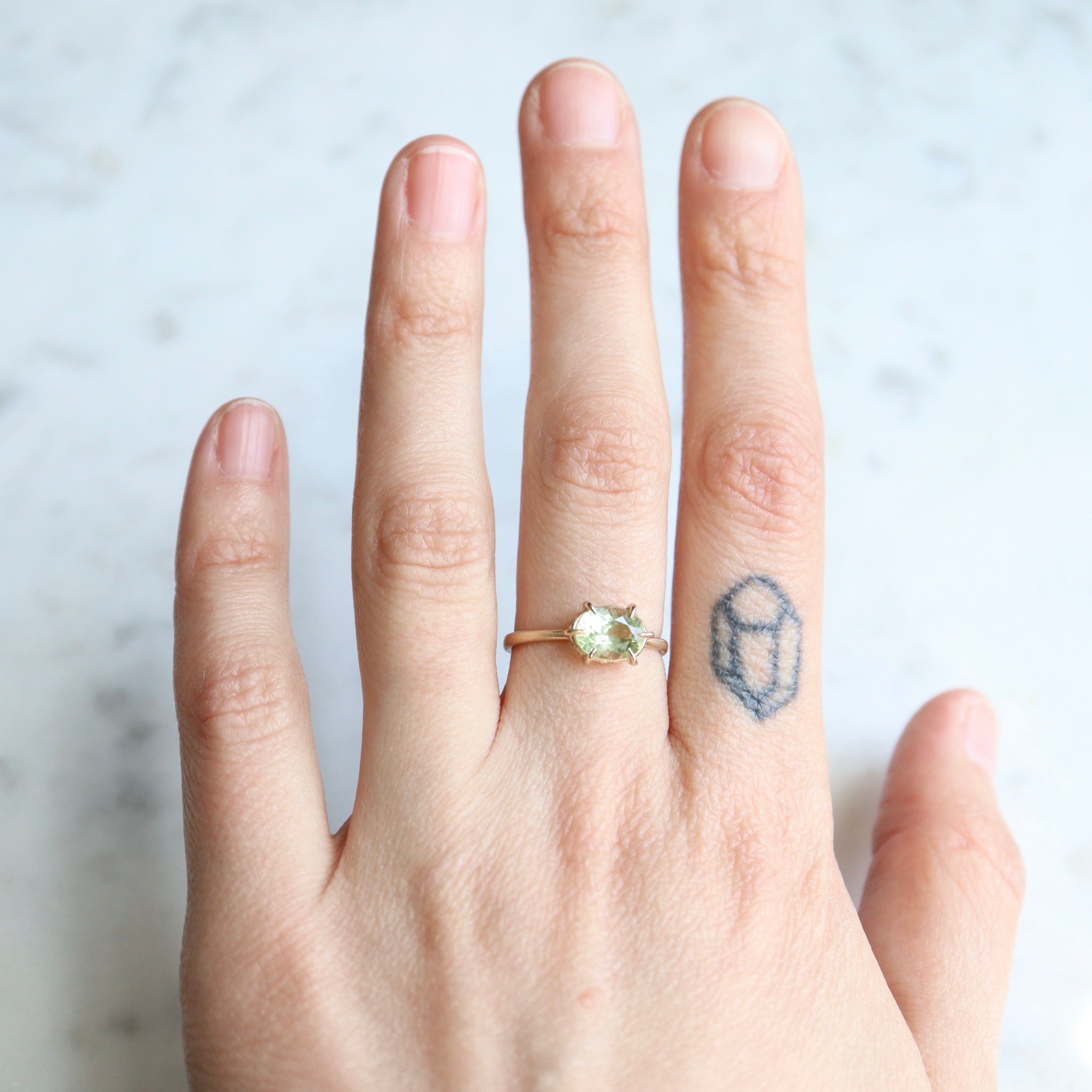 green oval tourmaline ring with gold prongs. on person.