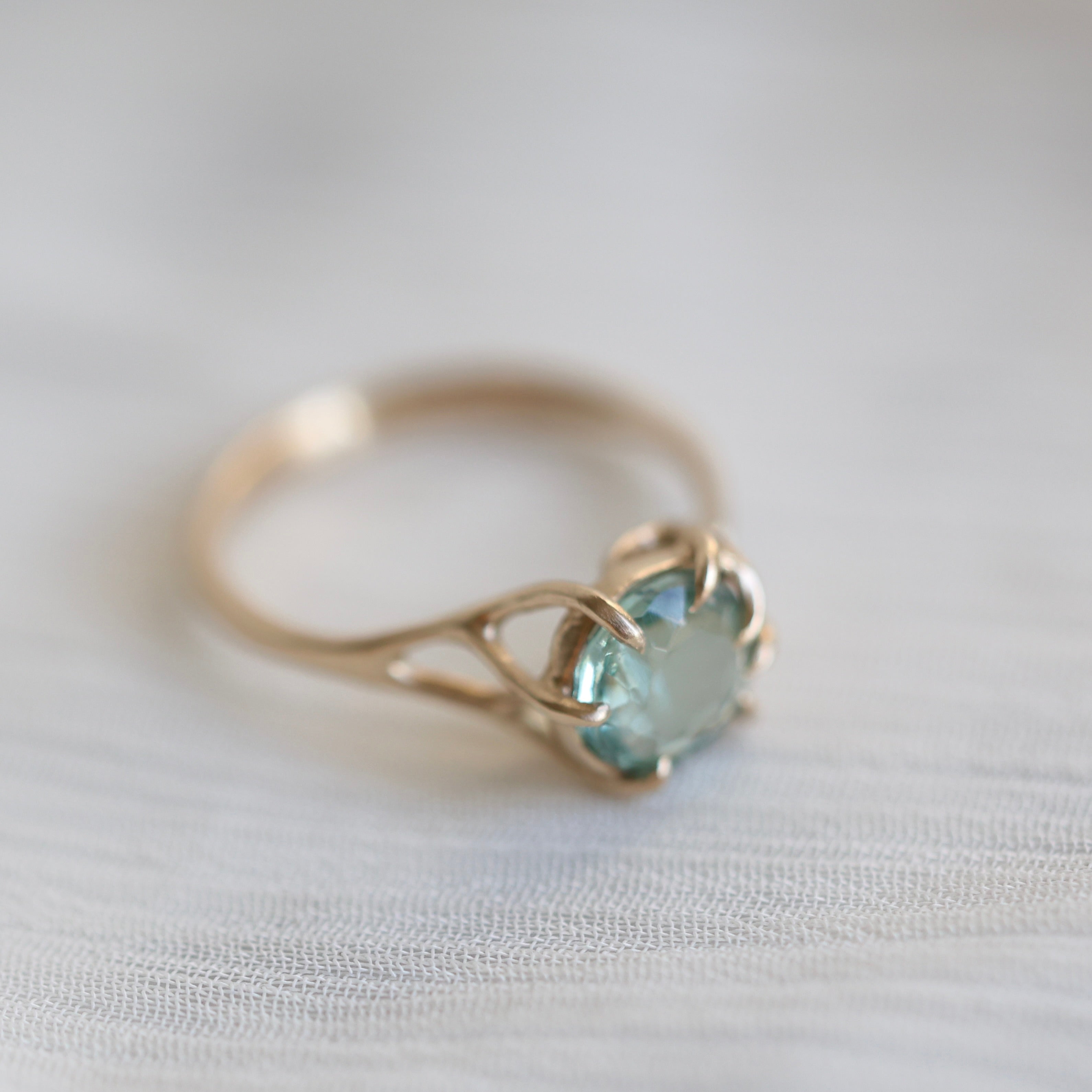 Gold ring with a mint green gemstone on a white fabric background