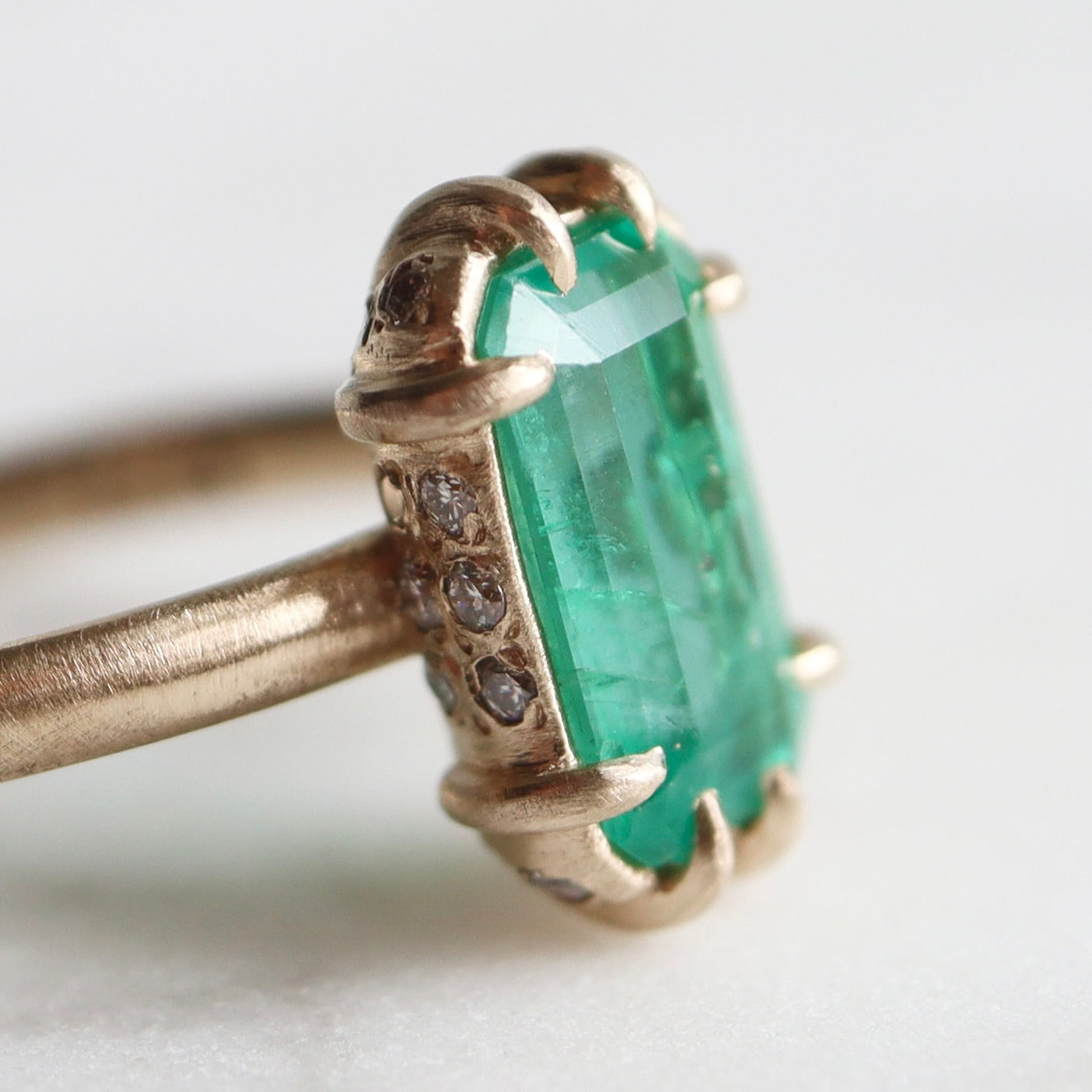 green emerald retangular stone set in gold ring with prongs- closeup to show diamonds