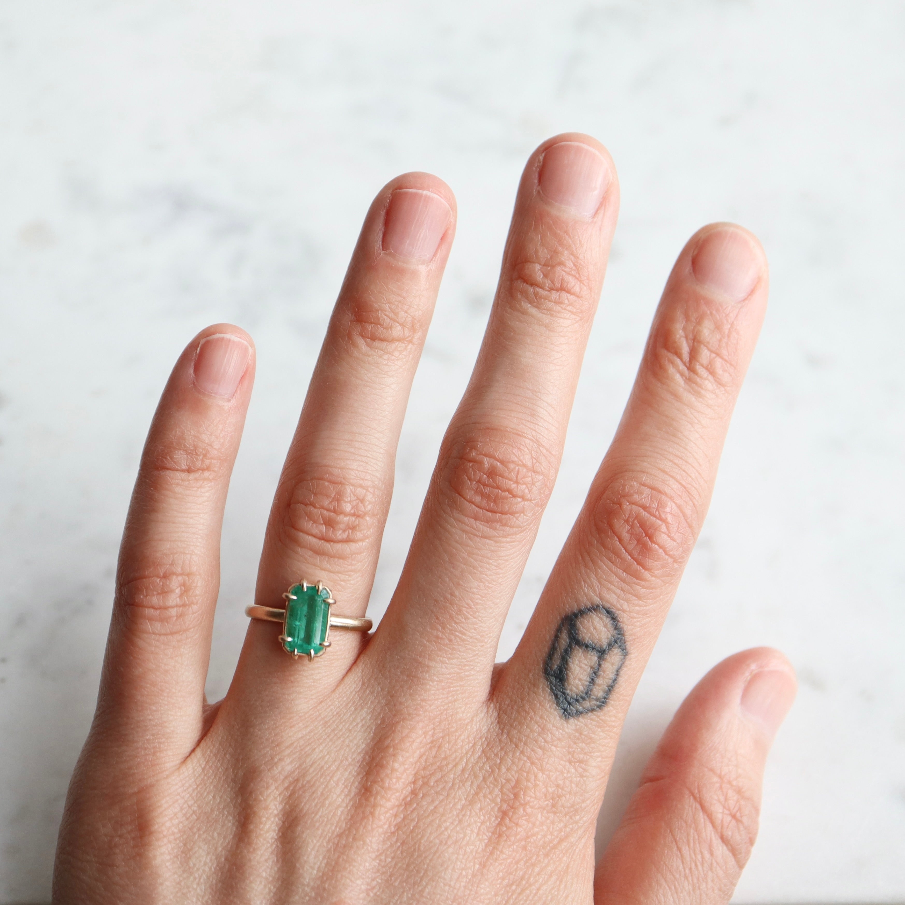green emerald retangular stone set in gold ring with prongs- on hand