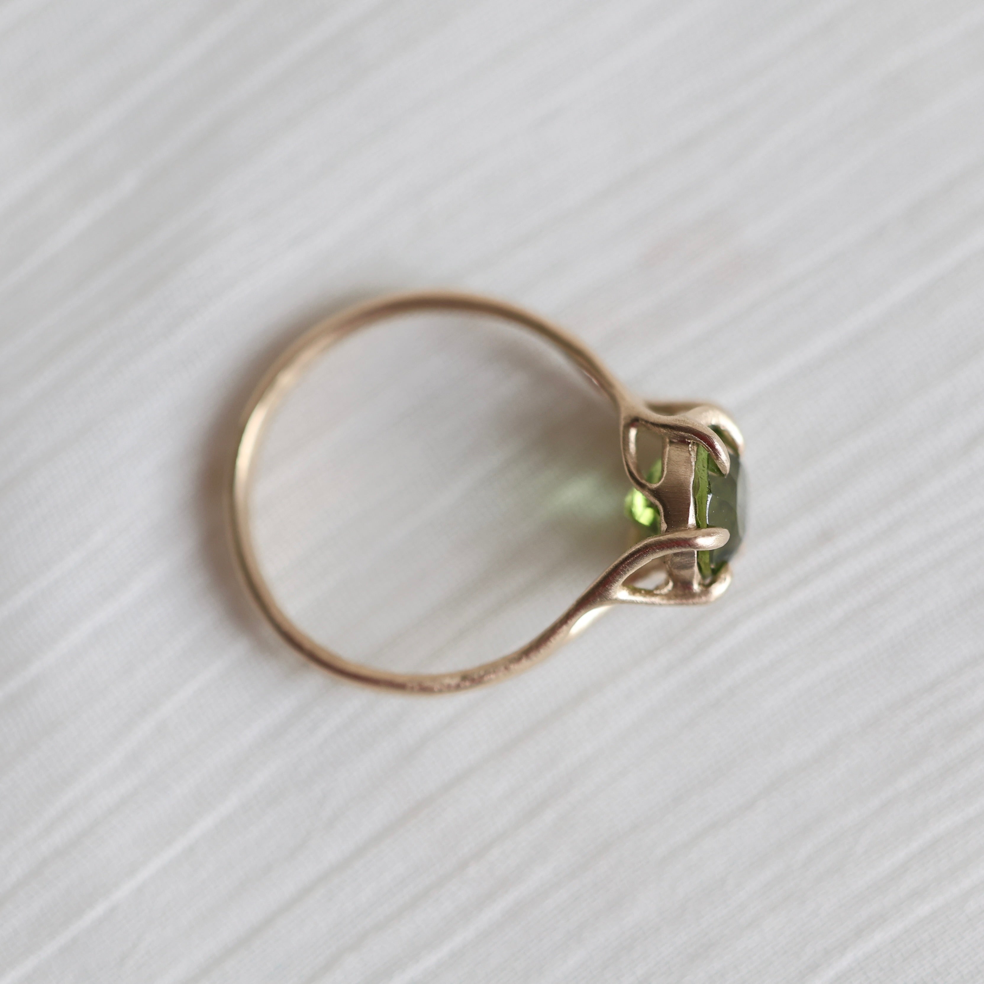 gold ring with green gemstone on pale fabric