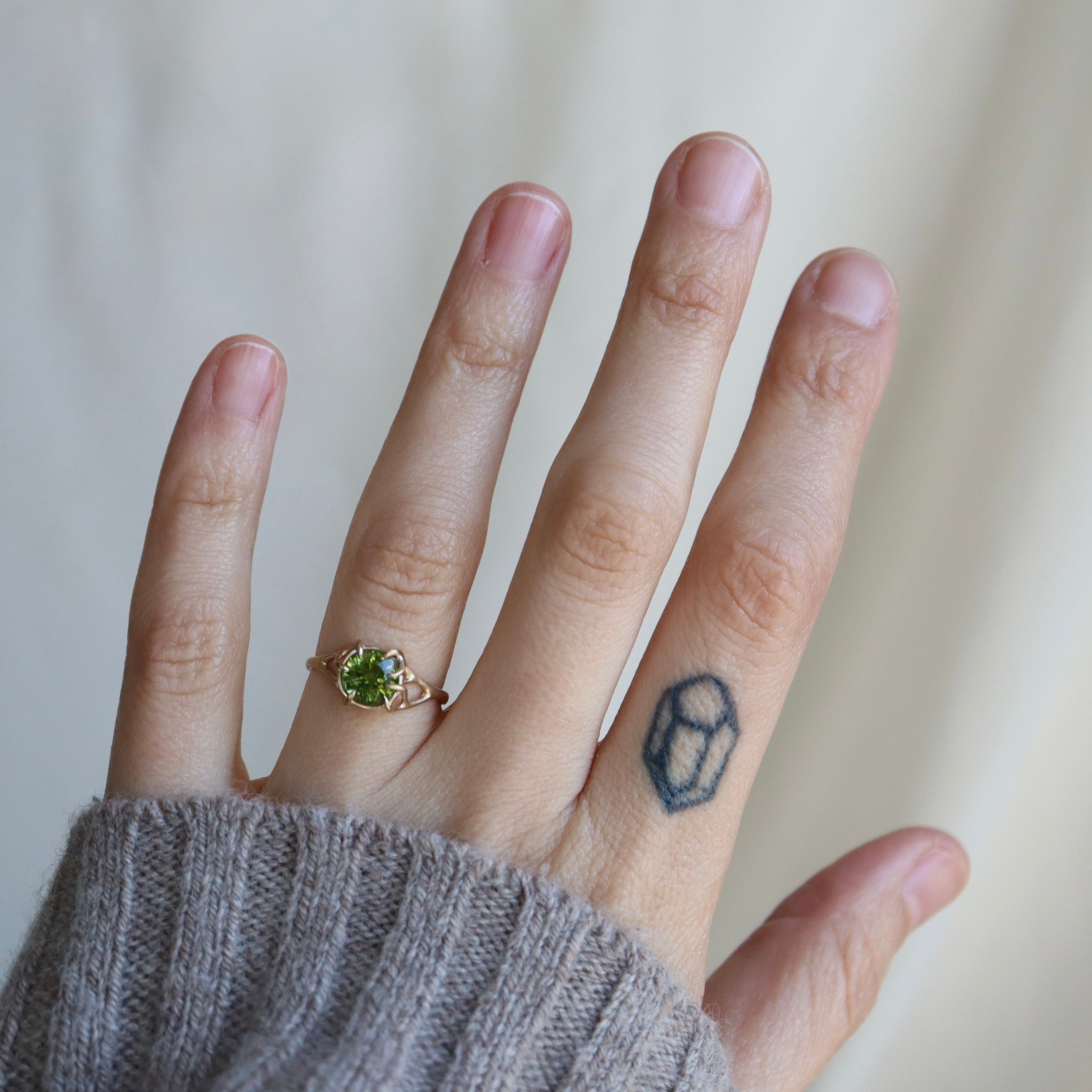 Hand wearing a ring with a green gemstone on a neutral background