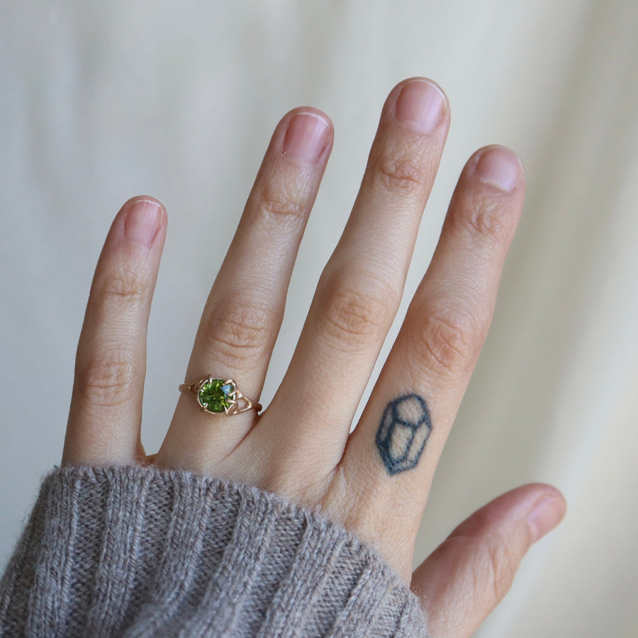 Hand wearing a ring with a green gemstone on a neutral background