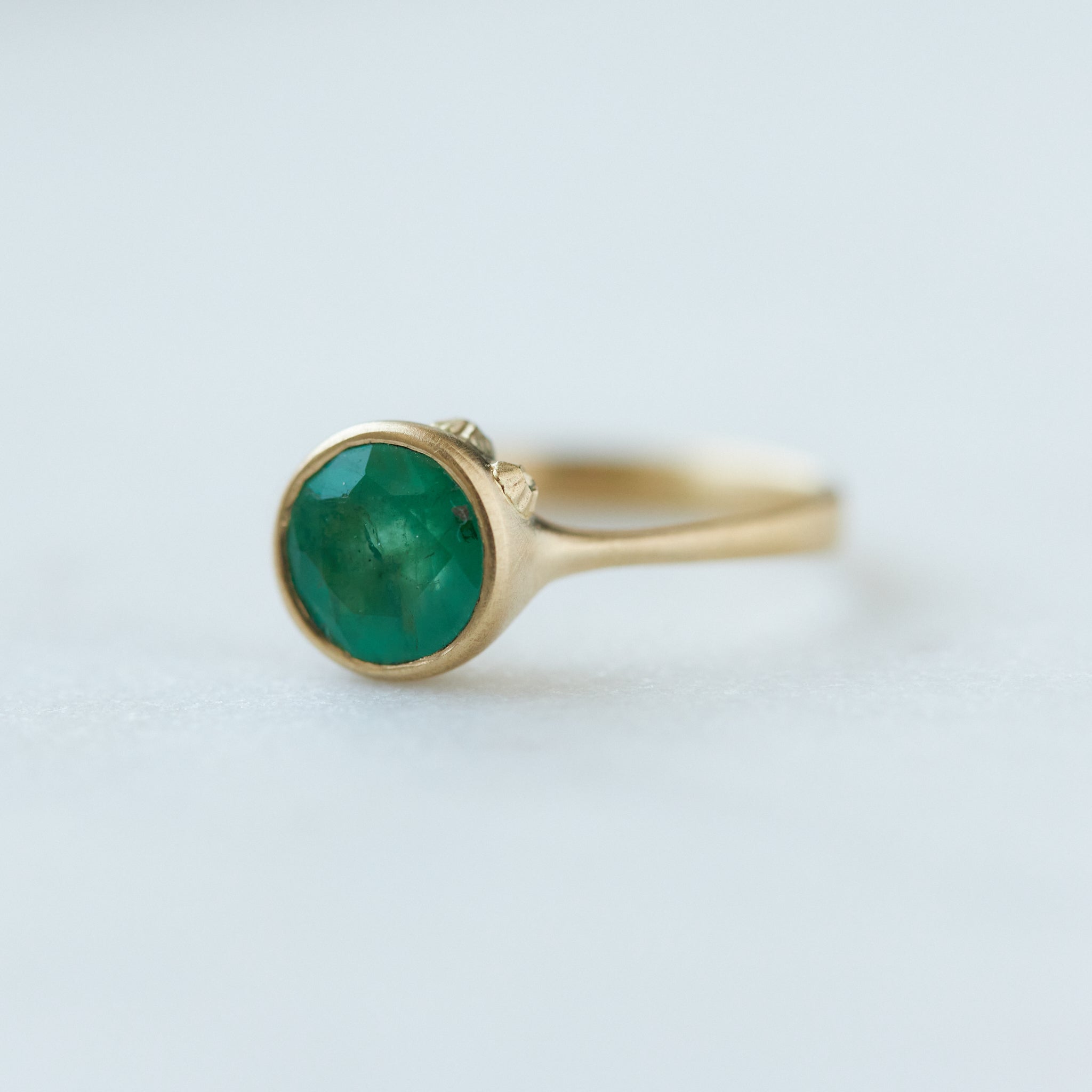 round rich green emerald is set in a gold bezel ring with gold barnacles. Side view.