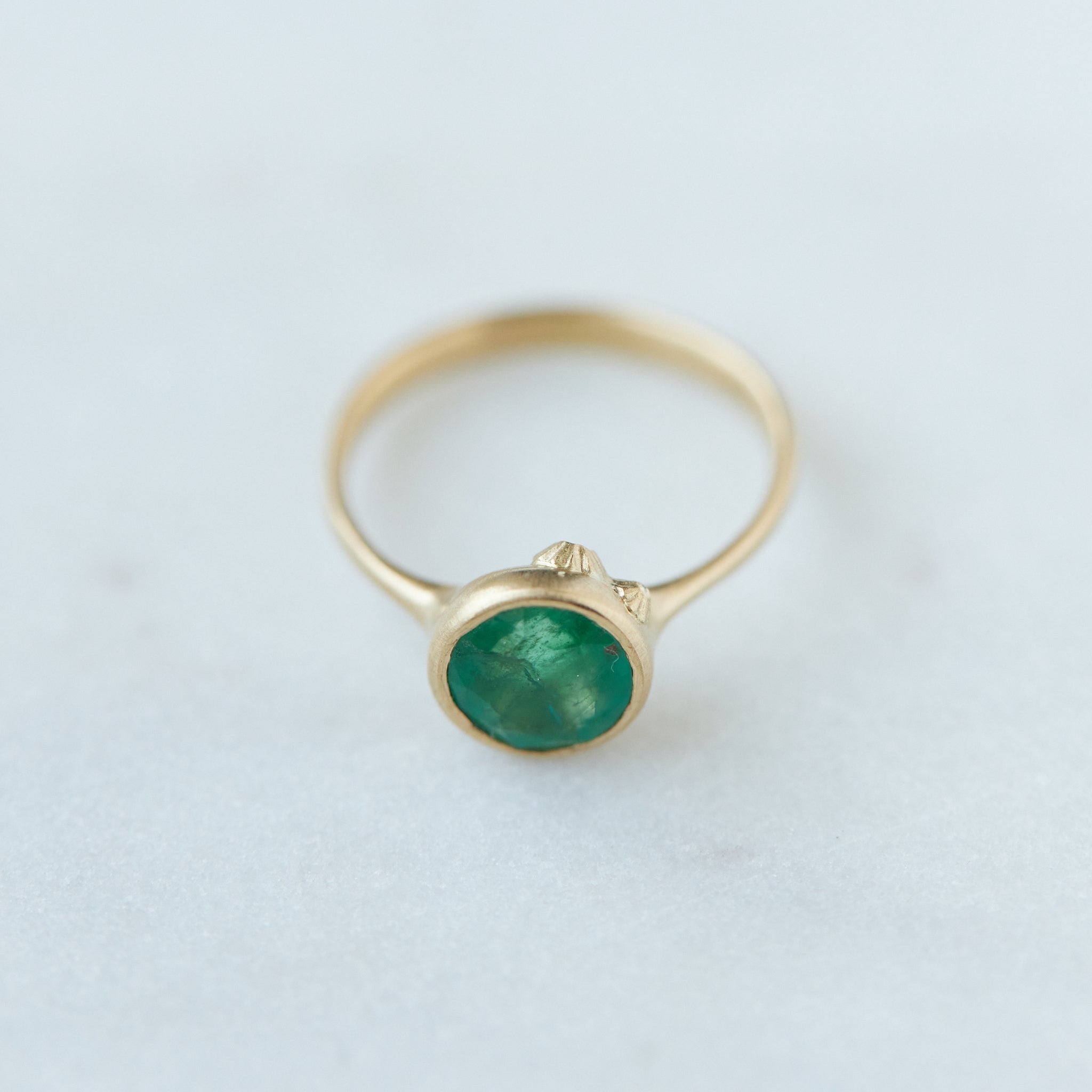 round rich green emerald is set in a gold bezel ring with gold barnacles. Top view.