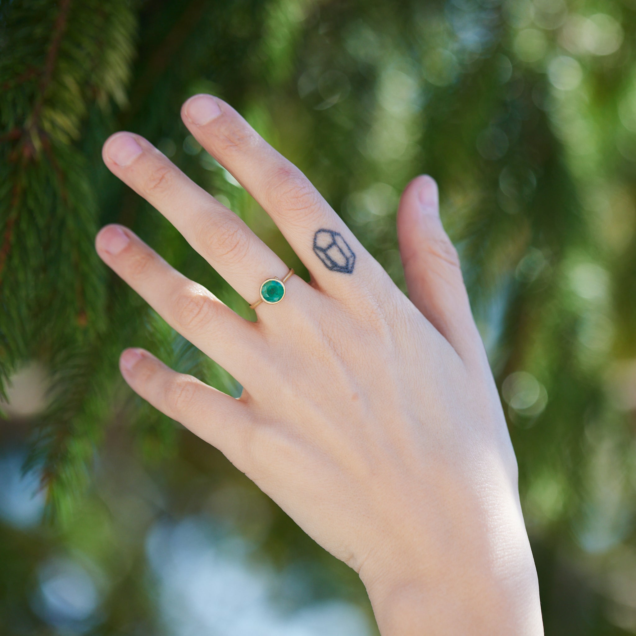 round rich green emerald is set in a gold bezel ring with gold barnacles. Photographed on person.