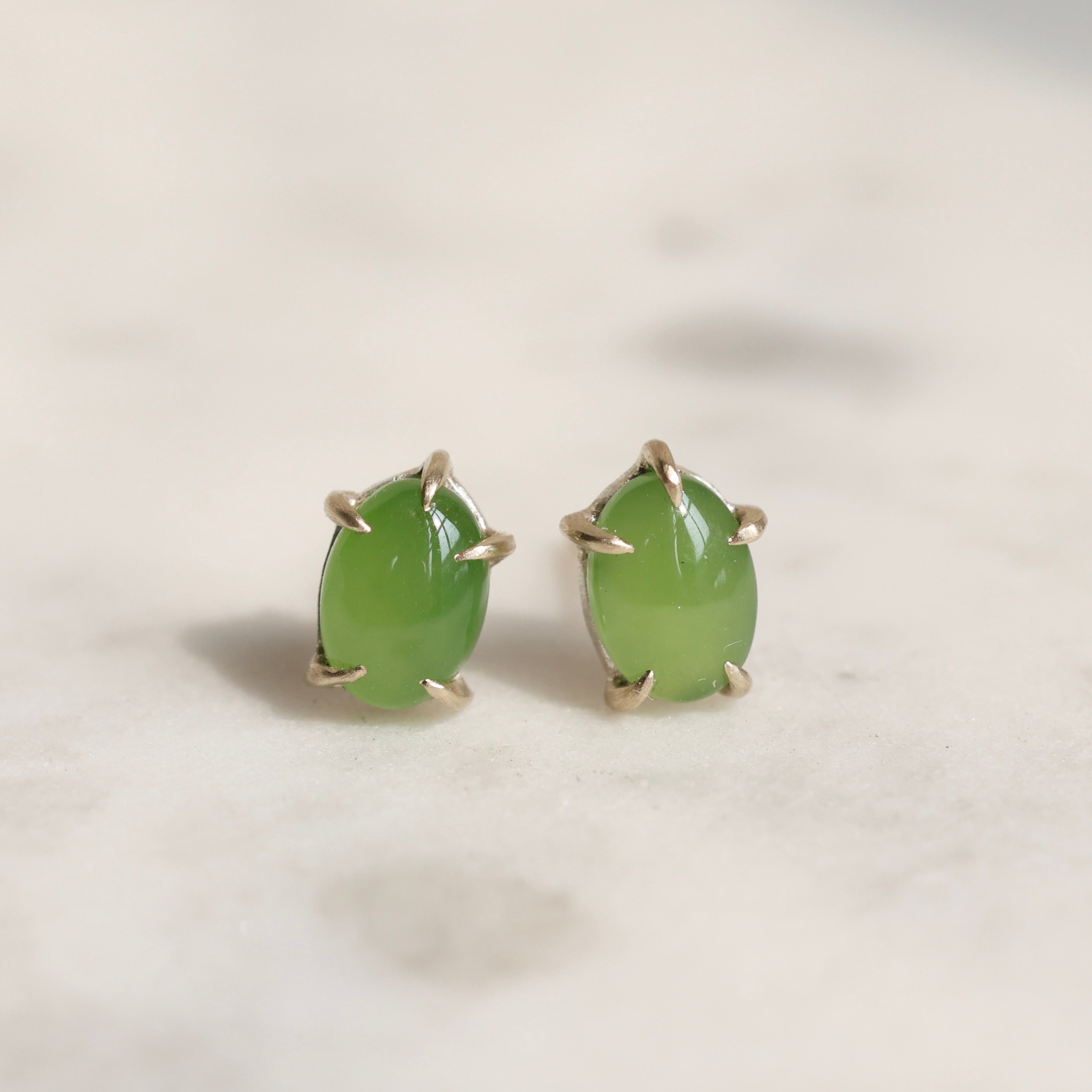 Pair of green jade cabochon stud earrings with five 14k yellow gold prongs on a light background.