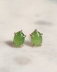 Pair of green jade cabochon stud earrings with five 14k yellow gold prongs on a light background.