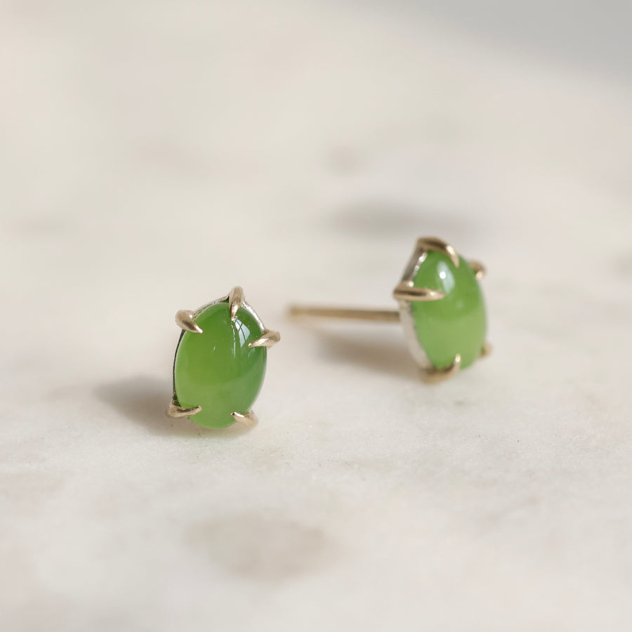 Pair of green jade cabochon stud earrings with five 14k yellow gold prongs on a light background.