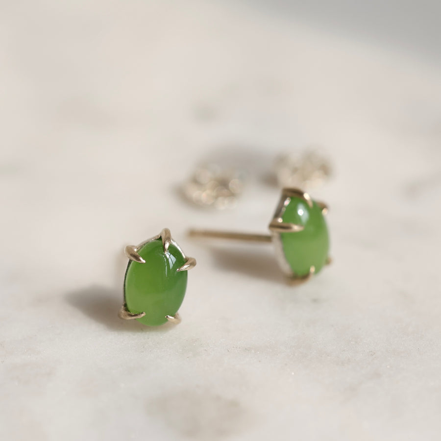 Pair of green jade cabochon stud earrings with five 14k yellow gold prongs on a light background.