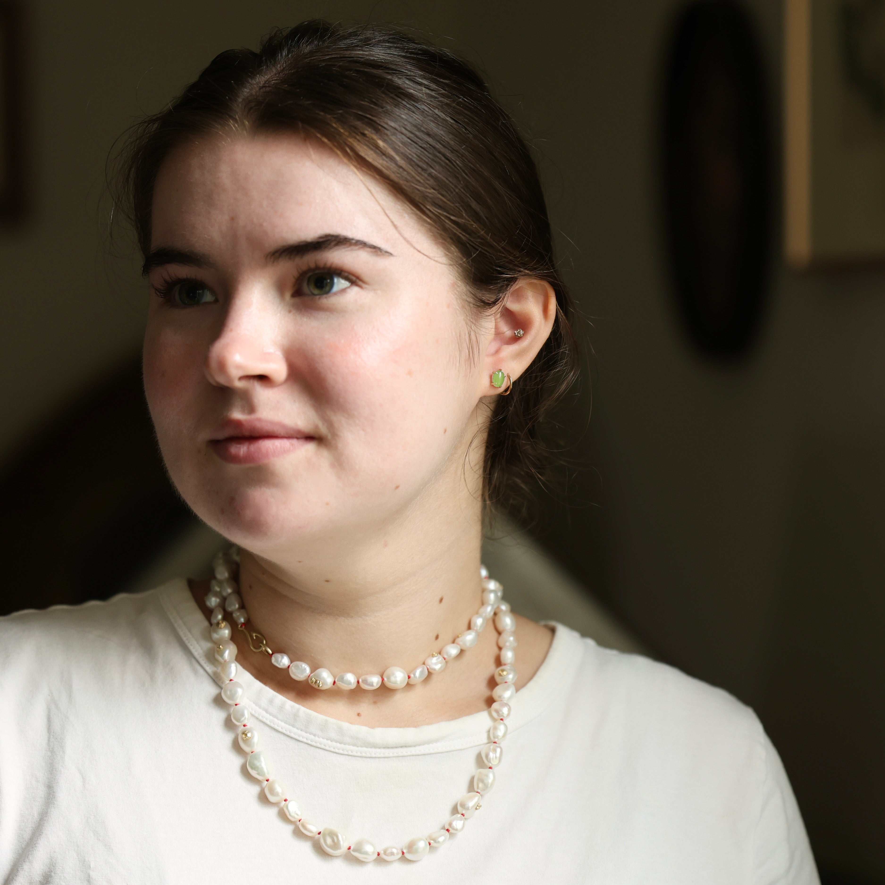 Pair of green jade cabochon stud earrings with five 14k yellow gold prongs and a double strand of white pearls shown worn on person. 