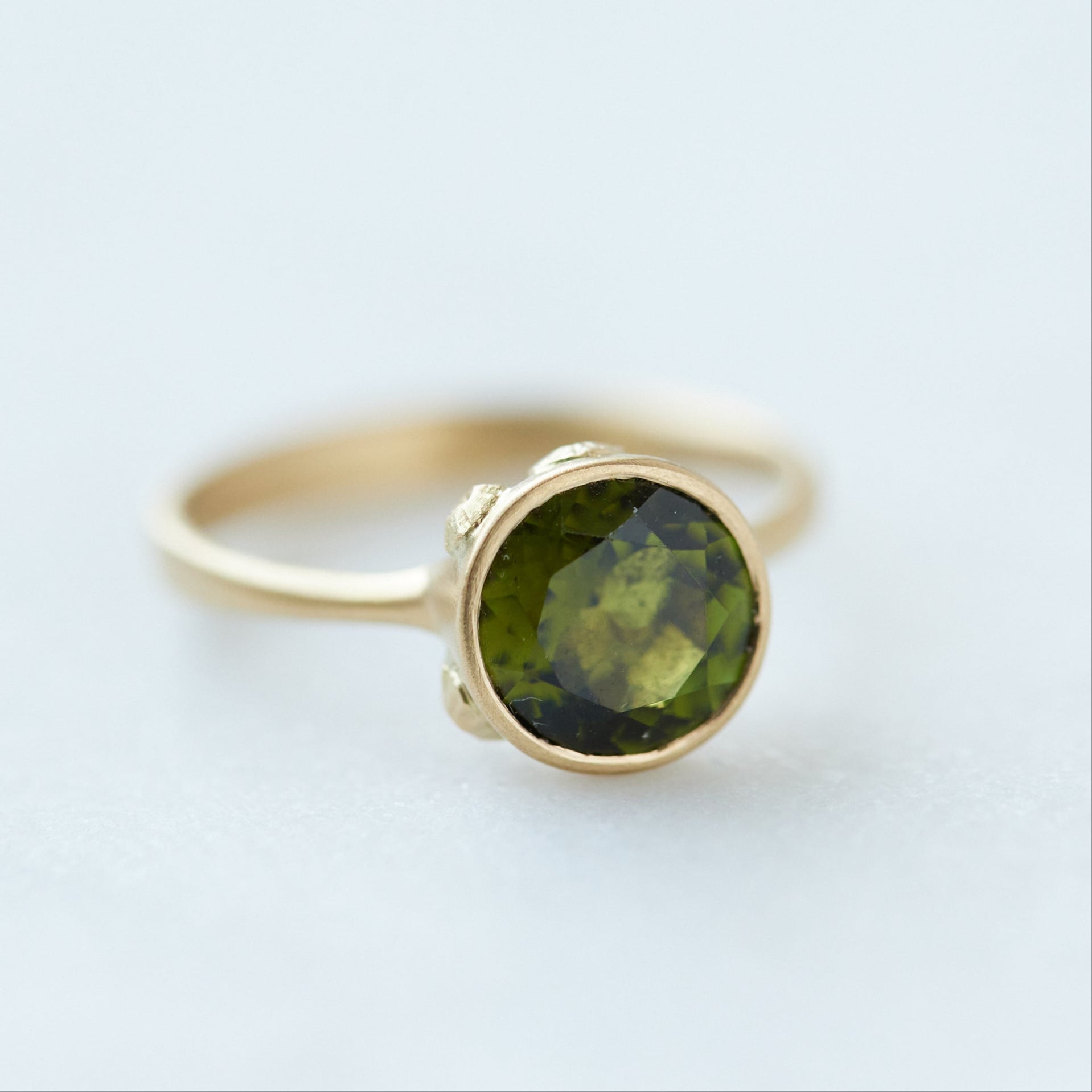 Round olive green tourmaline bezel set ring in gold with gold barnacles. 1/4 view.