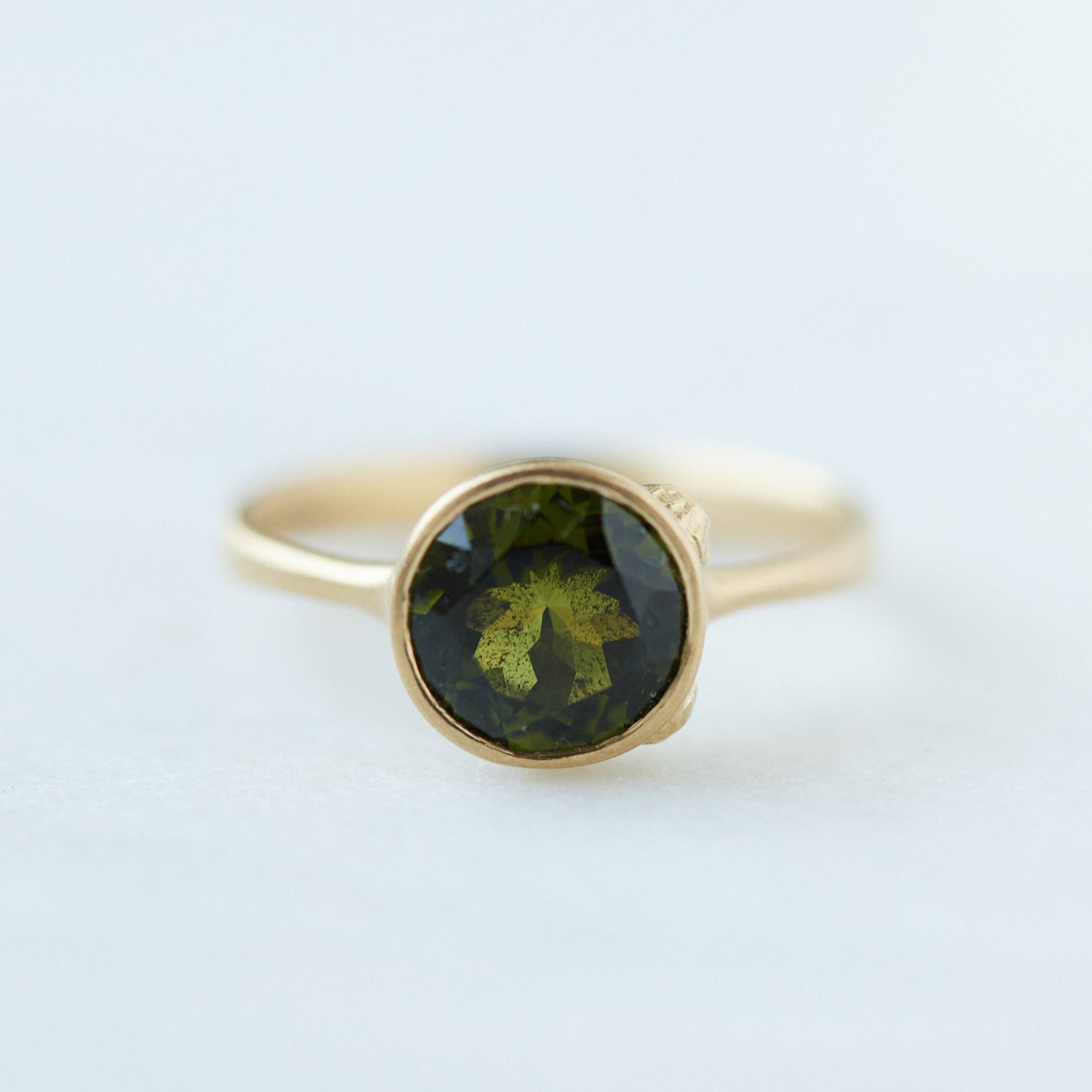 Round olive green tourmaline bezel set ring in gold with gold barnacles. Front view.