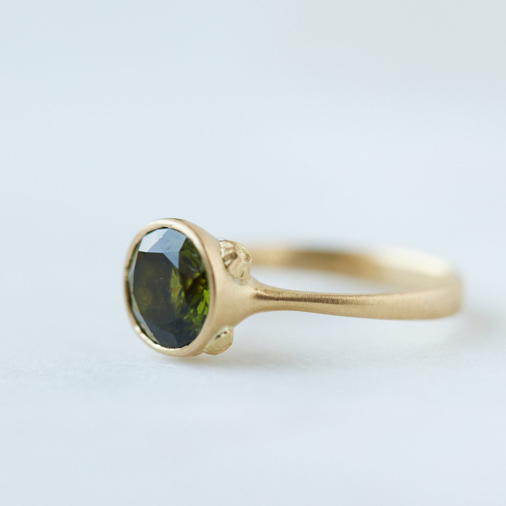 Round olive green tourmaline bezel set ring in gold with gold barnacles. Side view.