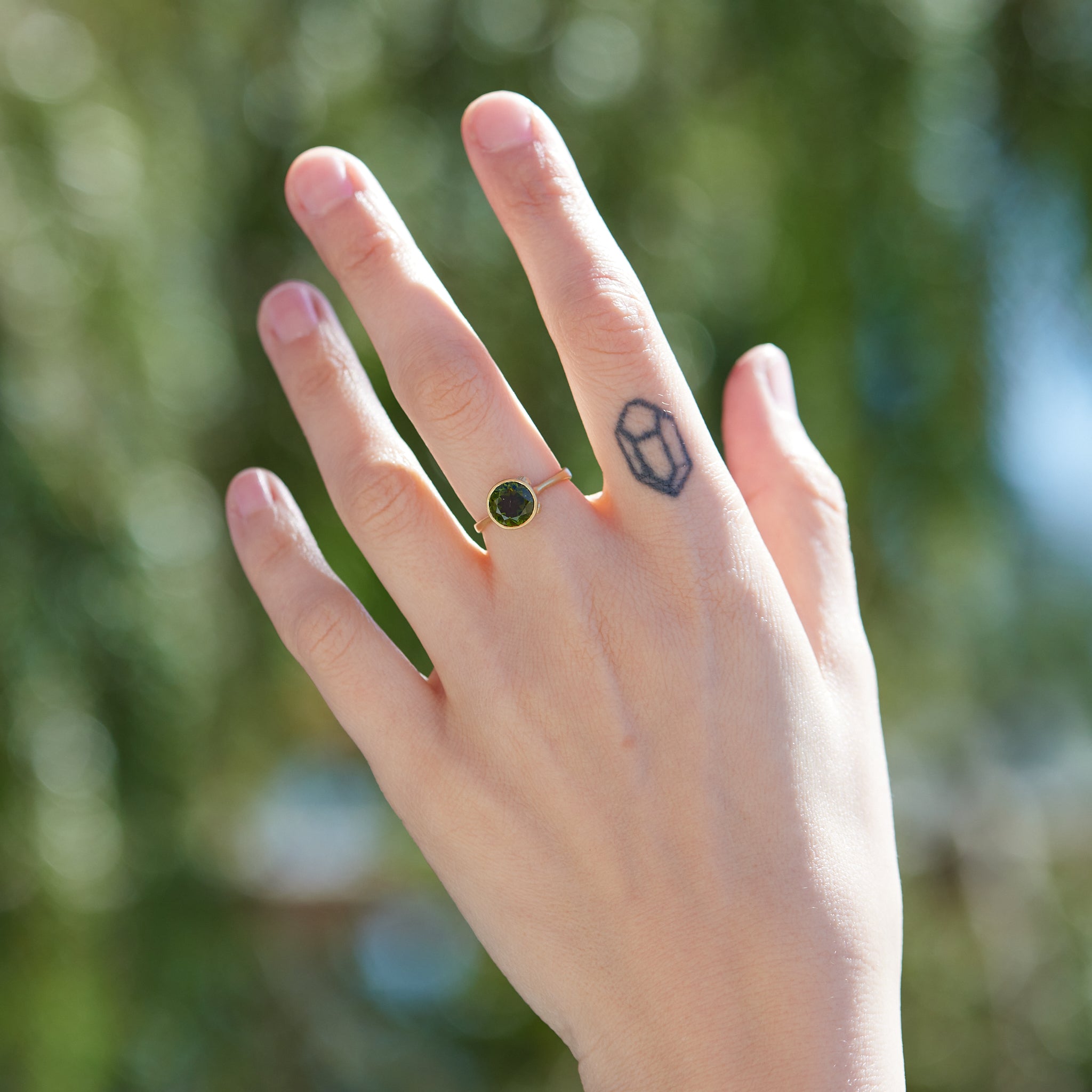 Round olive green tourmaline bezel set ring in gold with gold barnacles. Photographed on person.