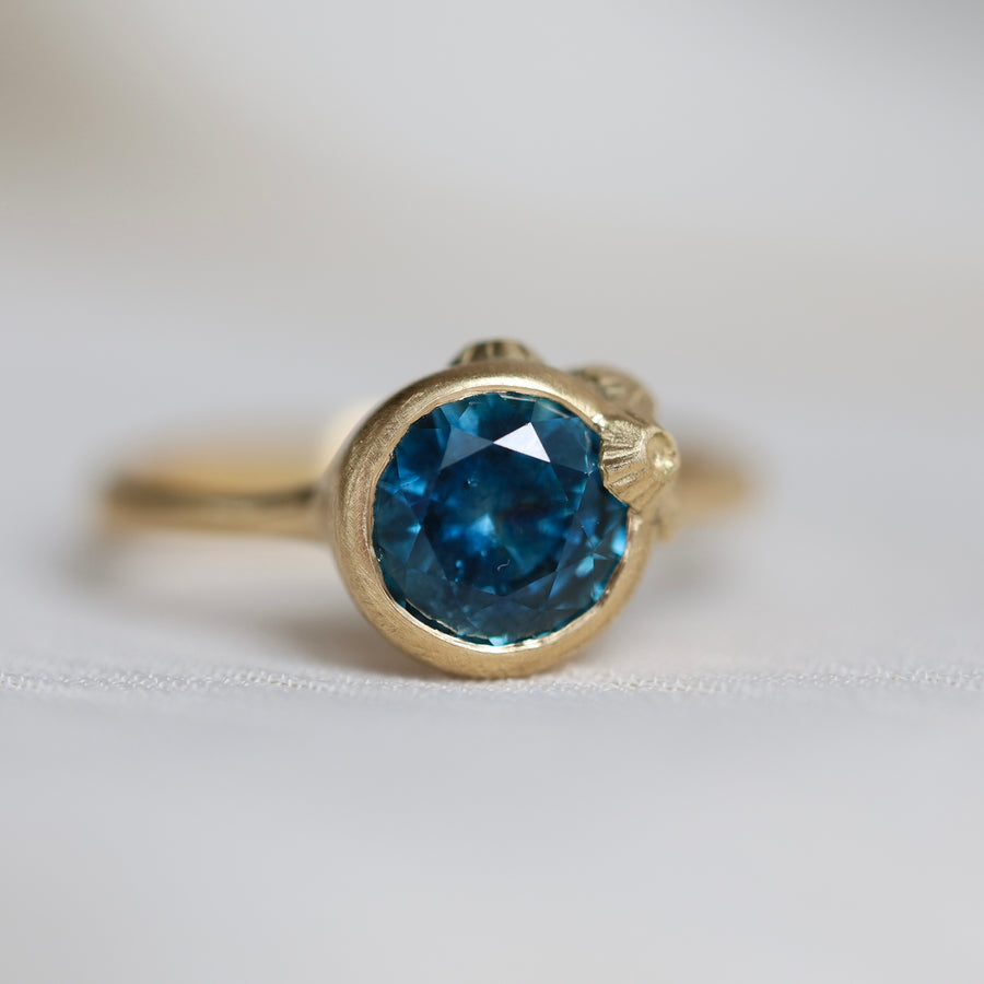Gold ring with a blue gemstone on a light gray background