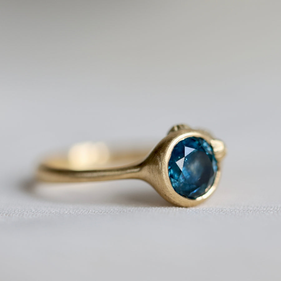 Gold ring with a blue gemstone on a light gray background