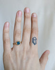 hand wearing a ring with a blue gemstone against a pale background