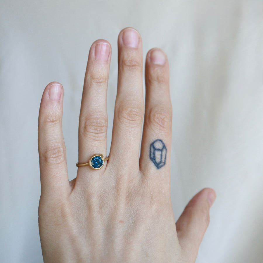 hand wearing a ring with a blue gemstone against a pale background