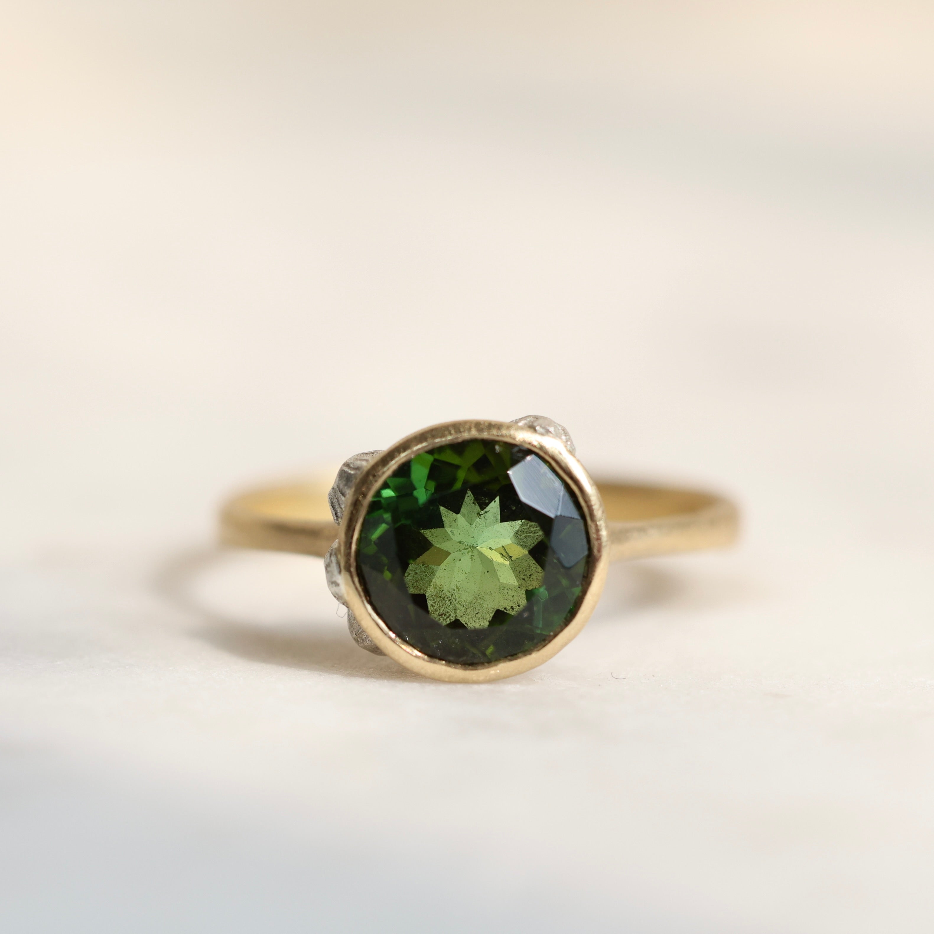 14k yellow gold bezel set ring with a green Tourmaline and bright sterling silver barnacles against a neutral background, front view.