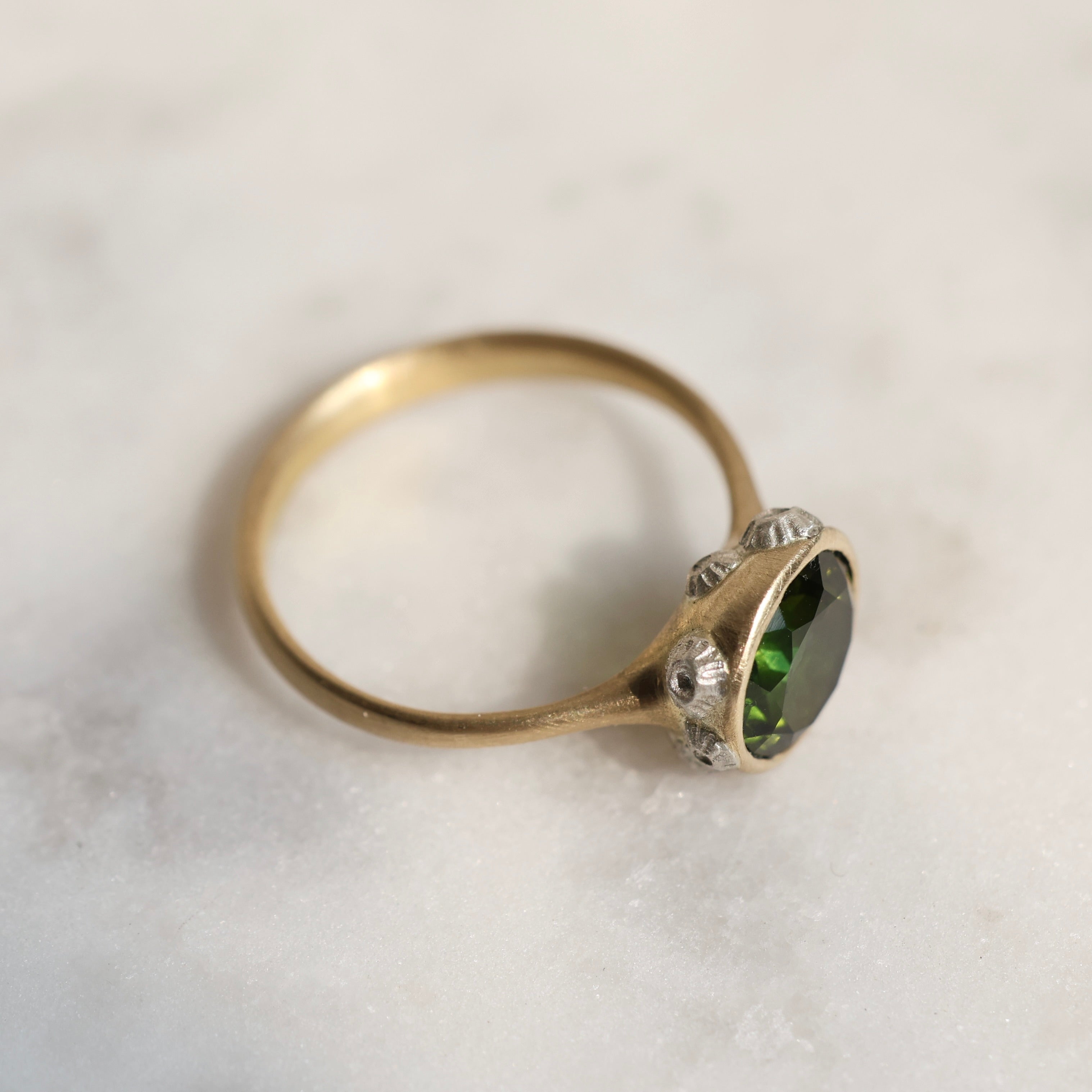 14k yellow gold bezel set ring with a green Tourmaline and bright sterling silver barnacles against a neutral background, side view.