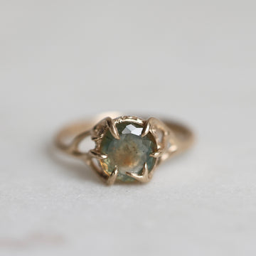 Gold ring with a multicolored gemstone on a light gray background