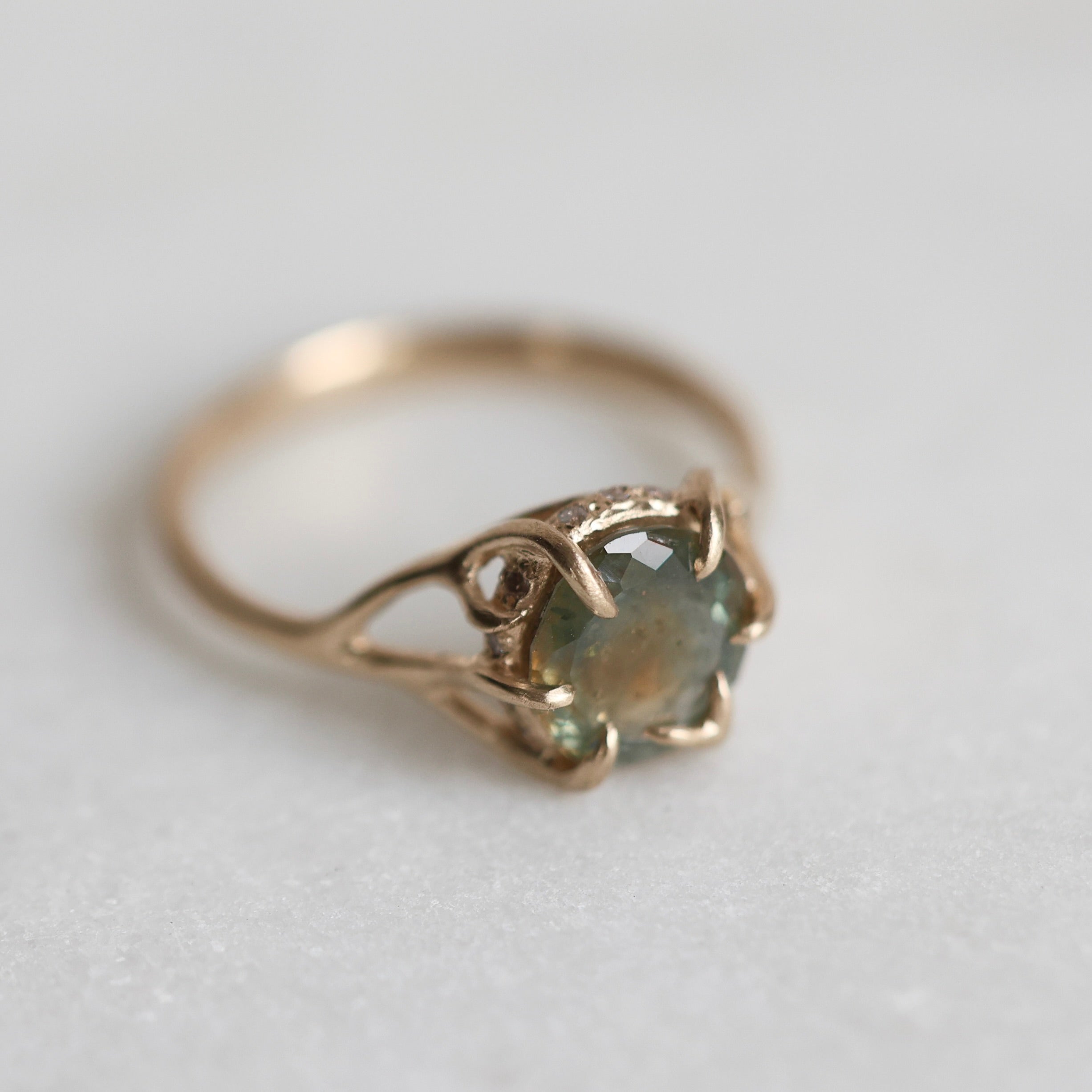 Gold ring with a multicolored gemstone on a light gray background