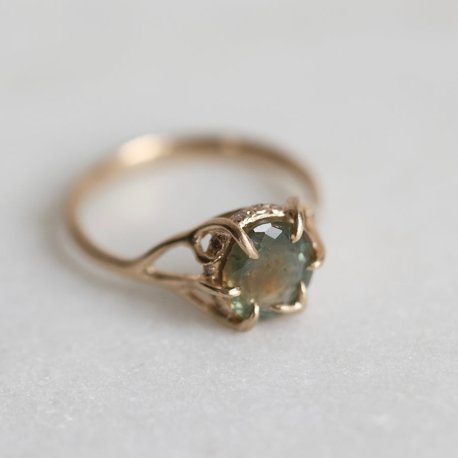 Gold ring with a multicolored gemstone on a light gray background