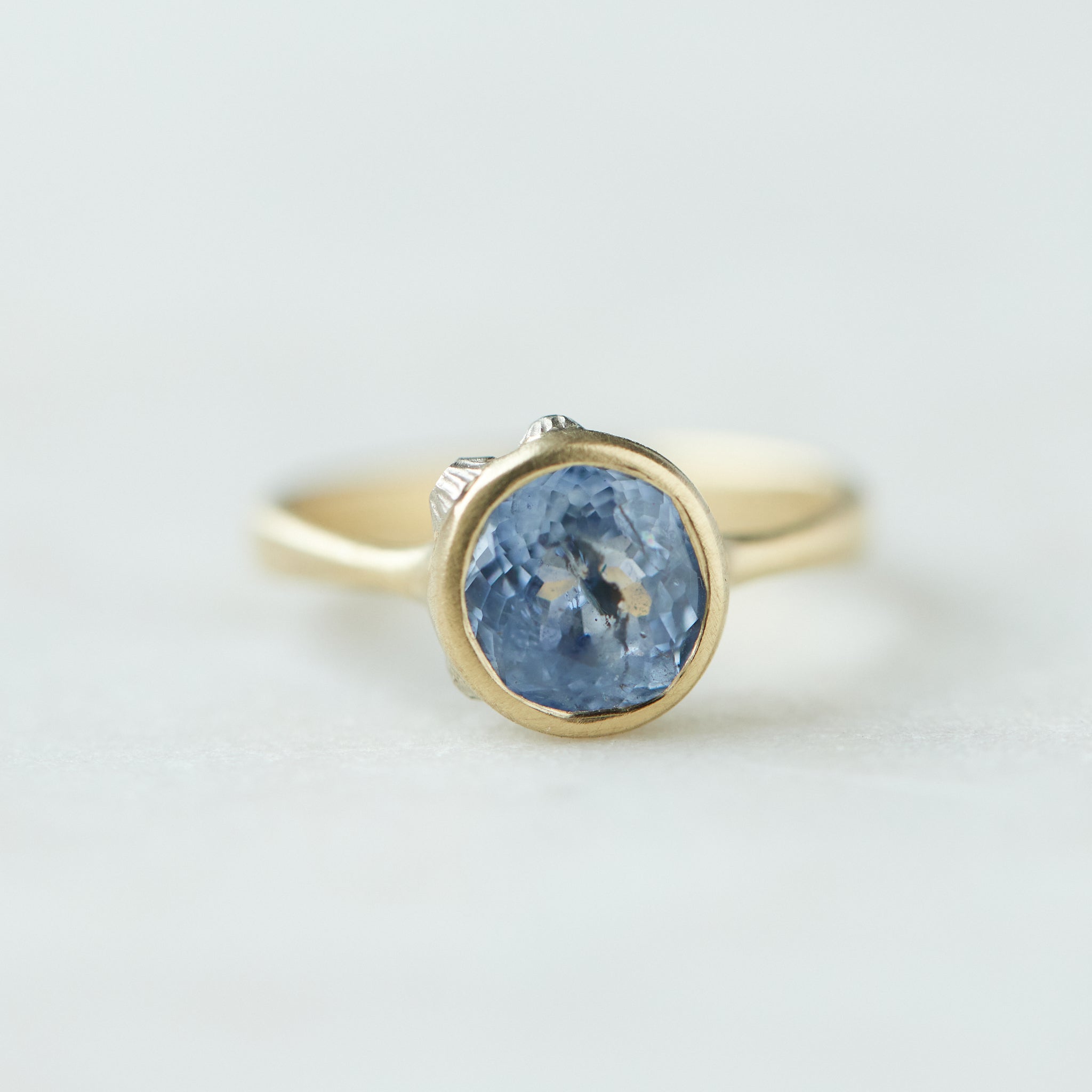 Periwinkle Montana sapphire in yellow gold bezel setting with hand-carved barnacles