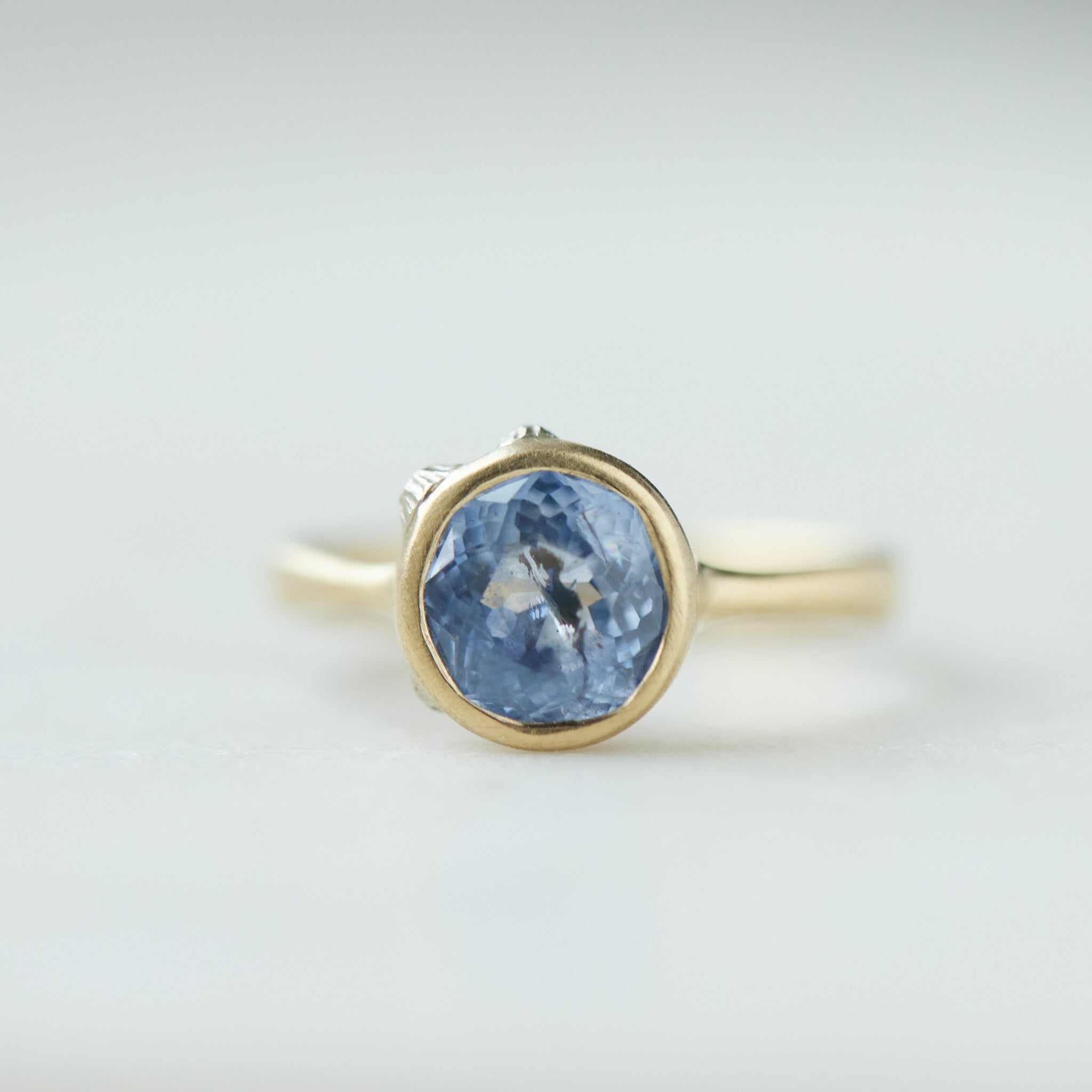 Periwinkle Montana sapphire in yellow gold bezel setting with hand-carved barnacles