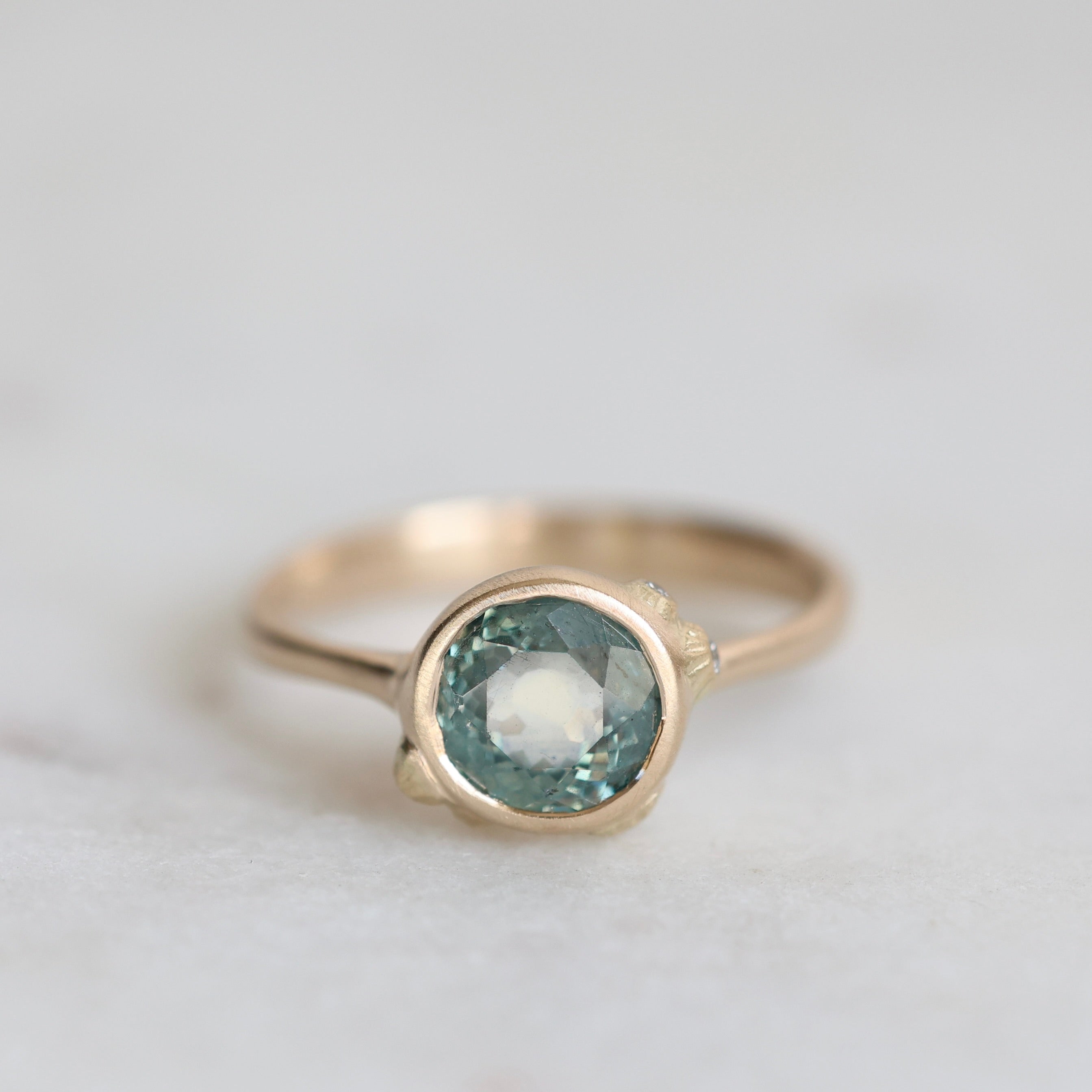 Gold ring with a blue gemstone on a light gray background