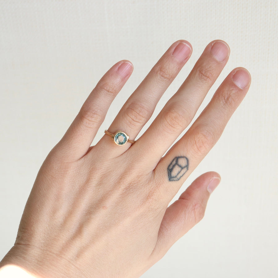Hand wearing a ring with a blue gemstone on a plain background