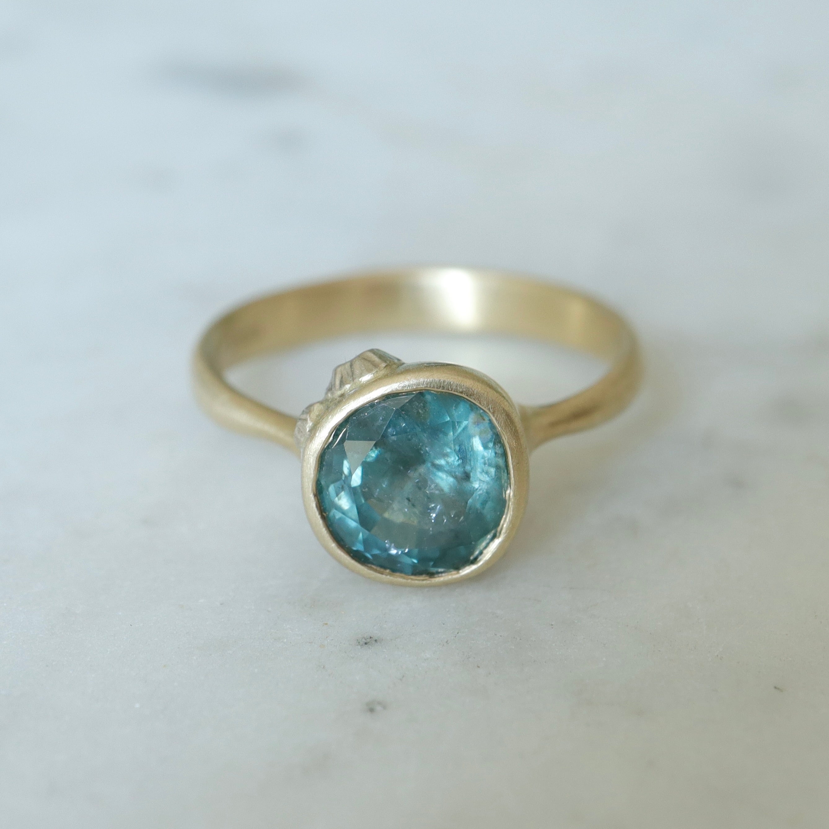 teal montana sapphire set within a bezel of a yellow gold ring, with white gold barnacles and diamonds
