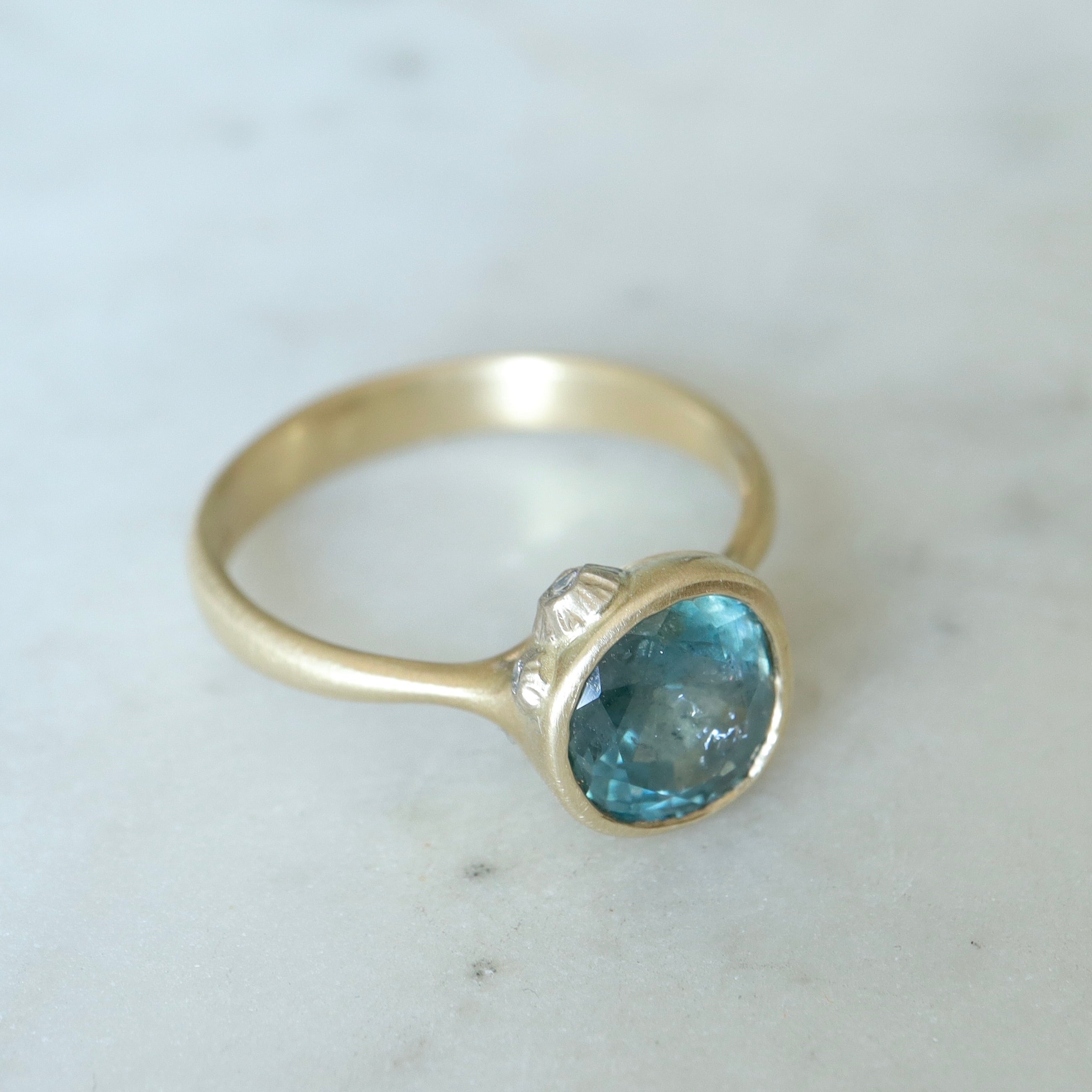teal montana sapphire set within a bezel of a yellow gold ring, with white gold barnacles and diamonds