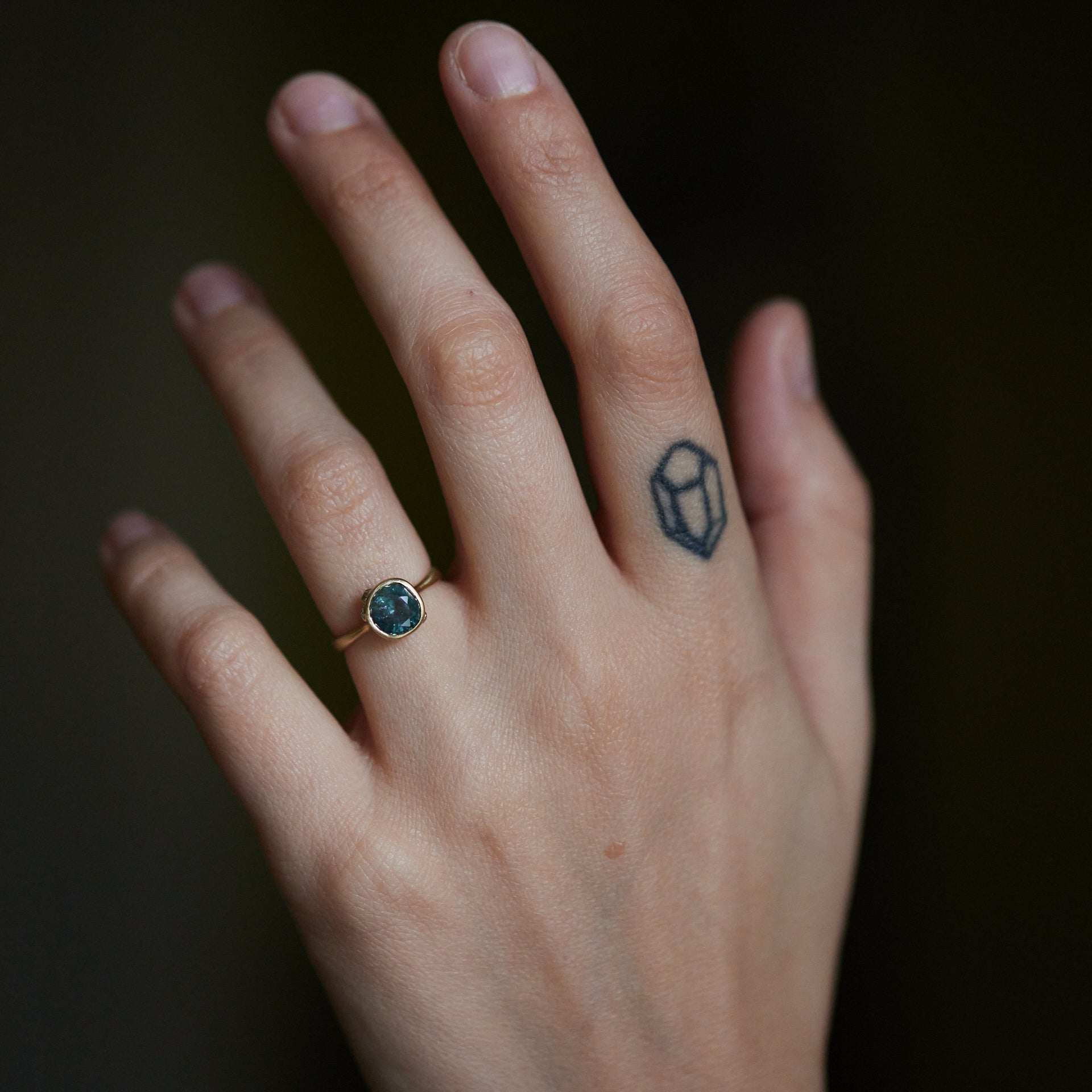 teal montana sapphire set within a bezel of a yellow gold ring, with white gold barnacles and diamonds- on hand