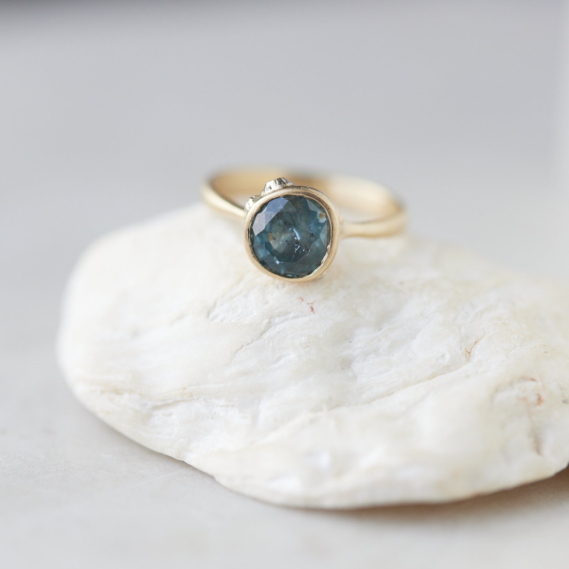 teal montana sapphire set within a bezel of a yellow gold ring, with white gold barnacles and diamonds