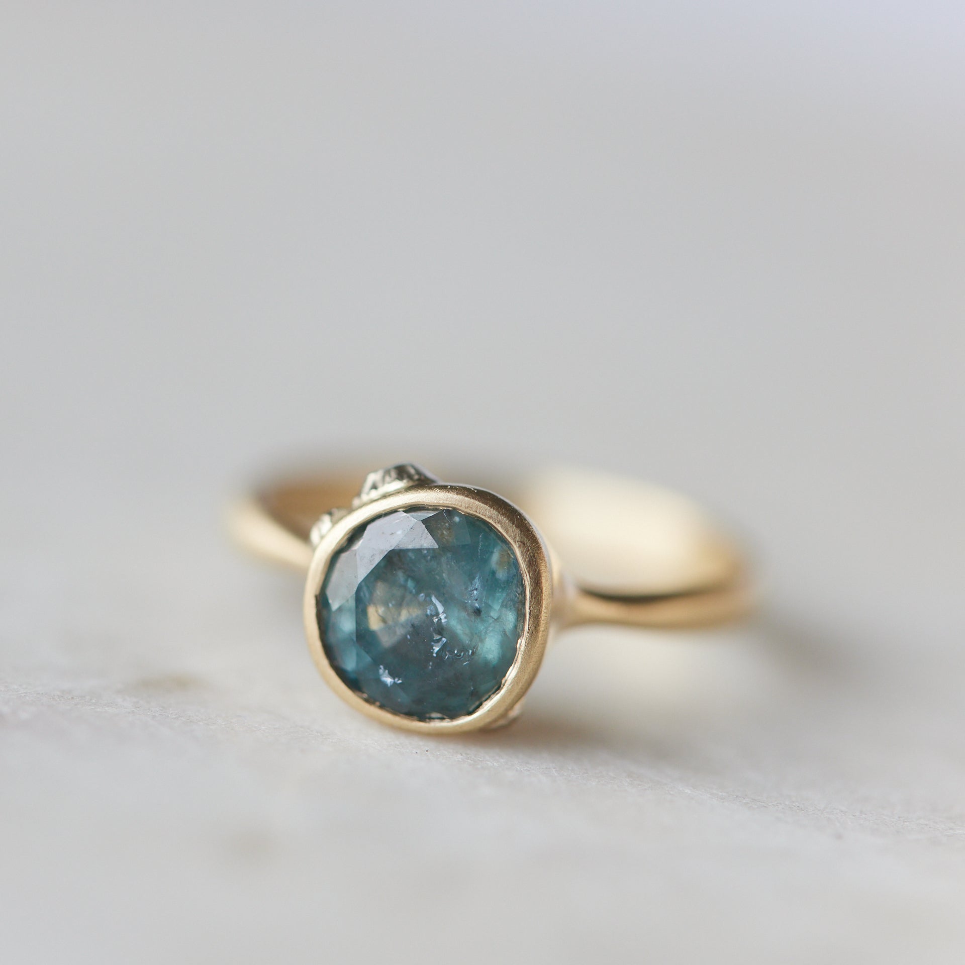 teal montana sapphire set within a bezel of a yellow gold ring, with white gold barnacles and diamonds