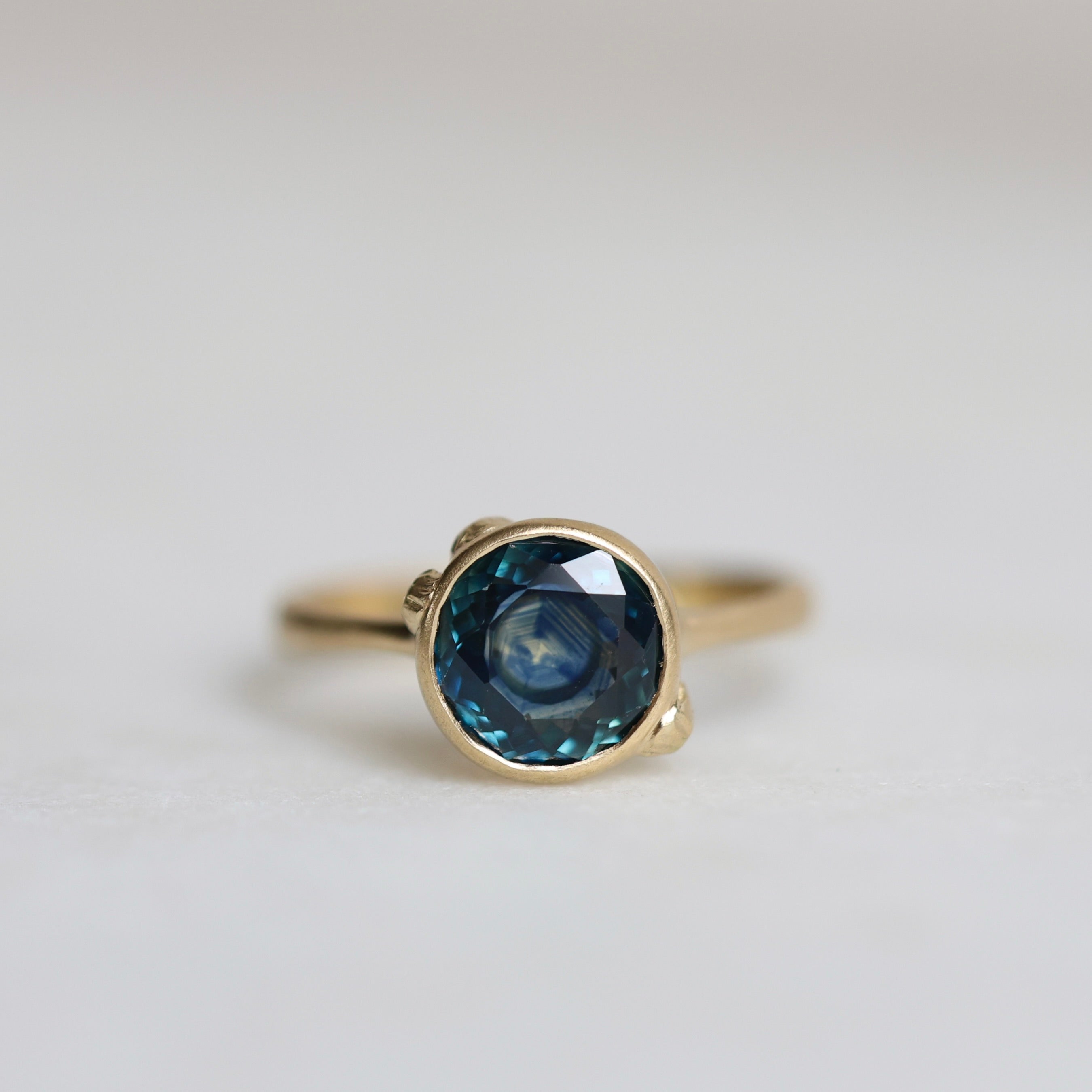 Gold ring with a blue gemstone on a light gray background