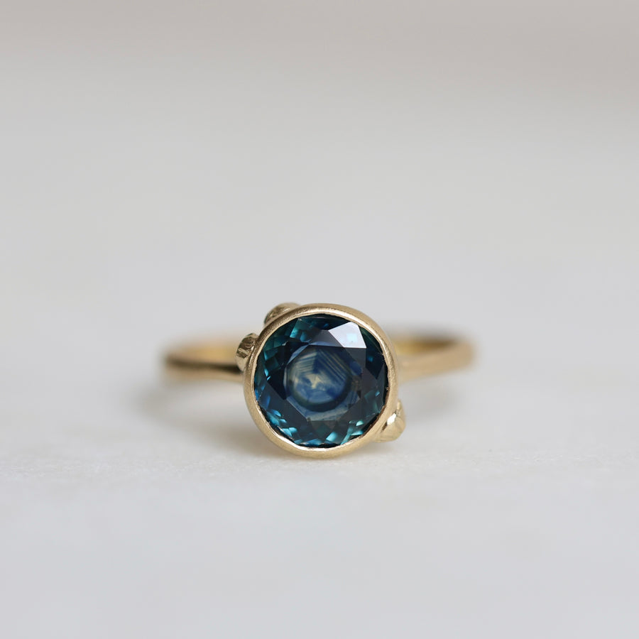 Gold ring with a blue gemstone on a light gray background