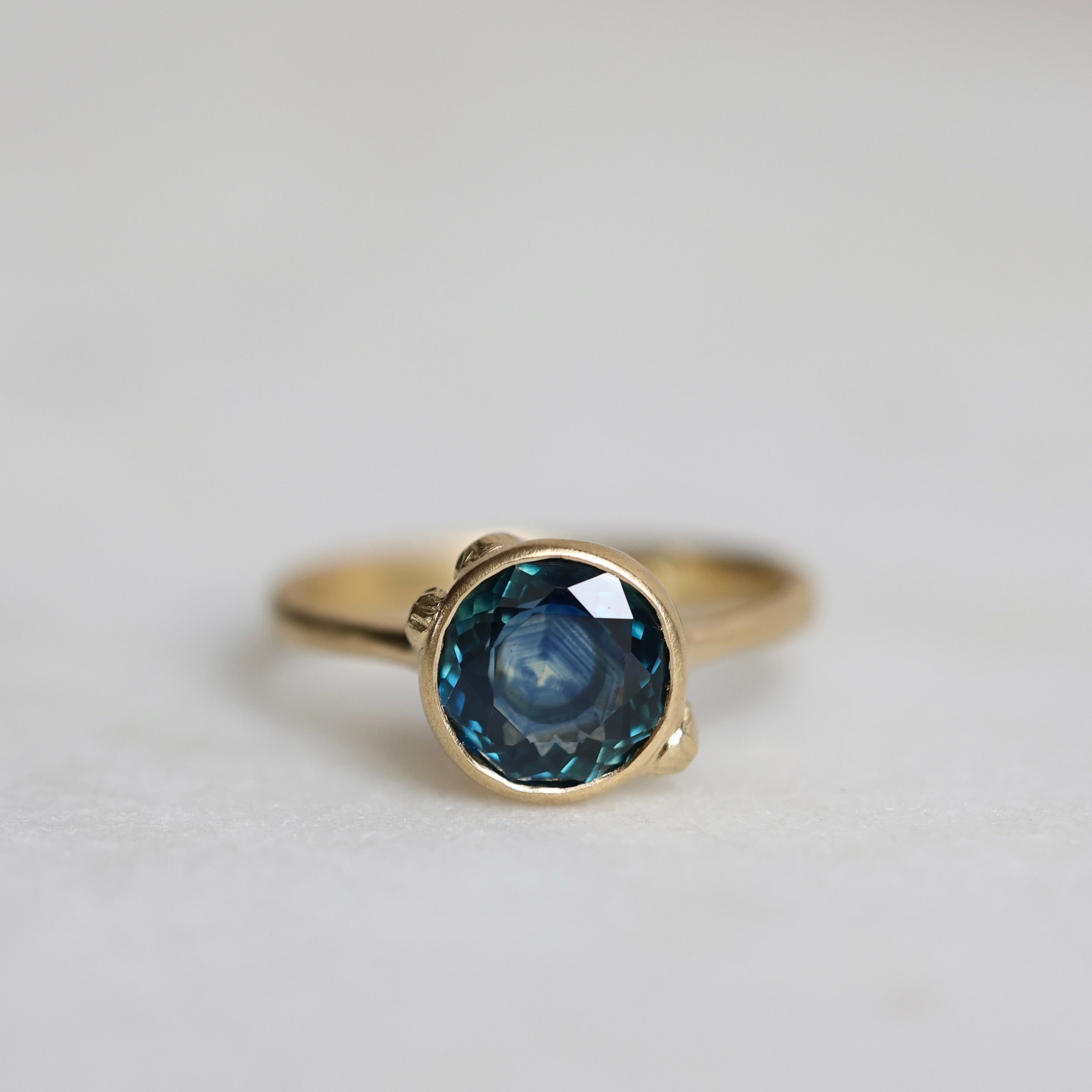 Gold ring with a blue gemstone on a light gray background